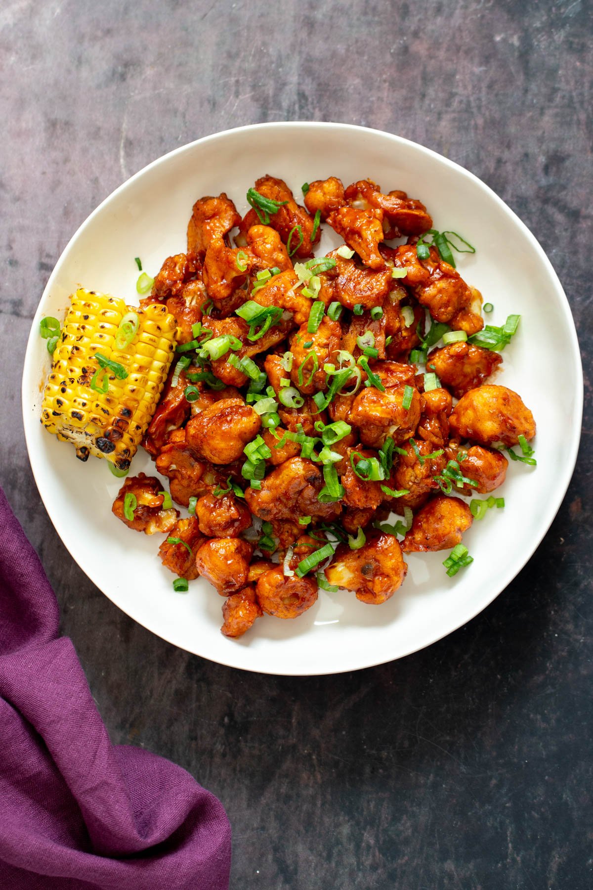 cauliflower wings  vegan baked beet battered cauliflower wings coated in bbq sauce served on a white plate with corn on the cob