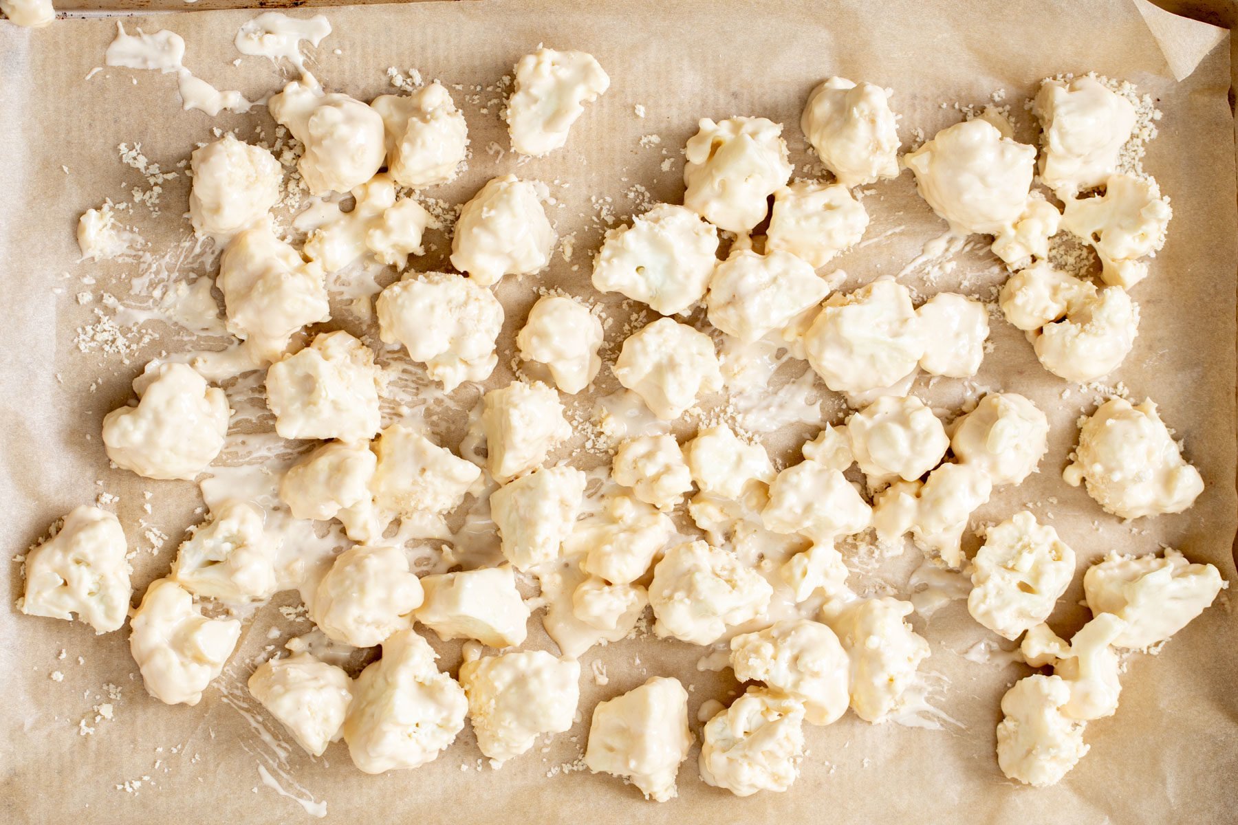 battered cauliflower florets on a lined baking sheet