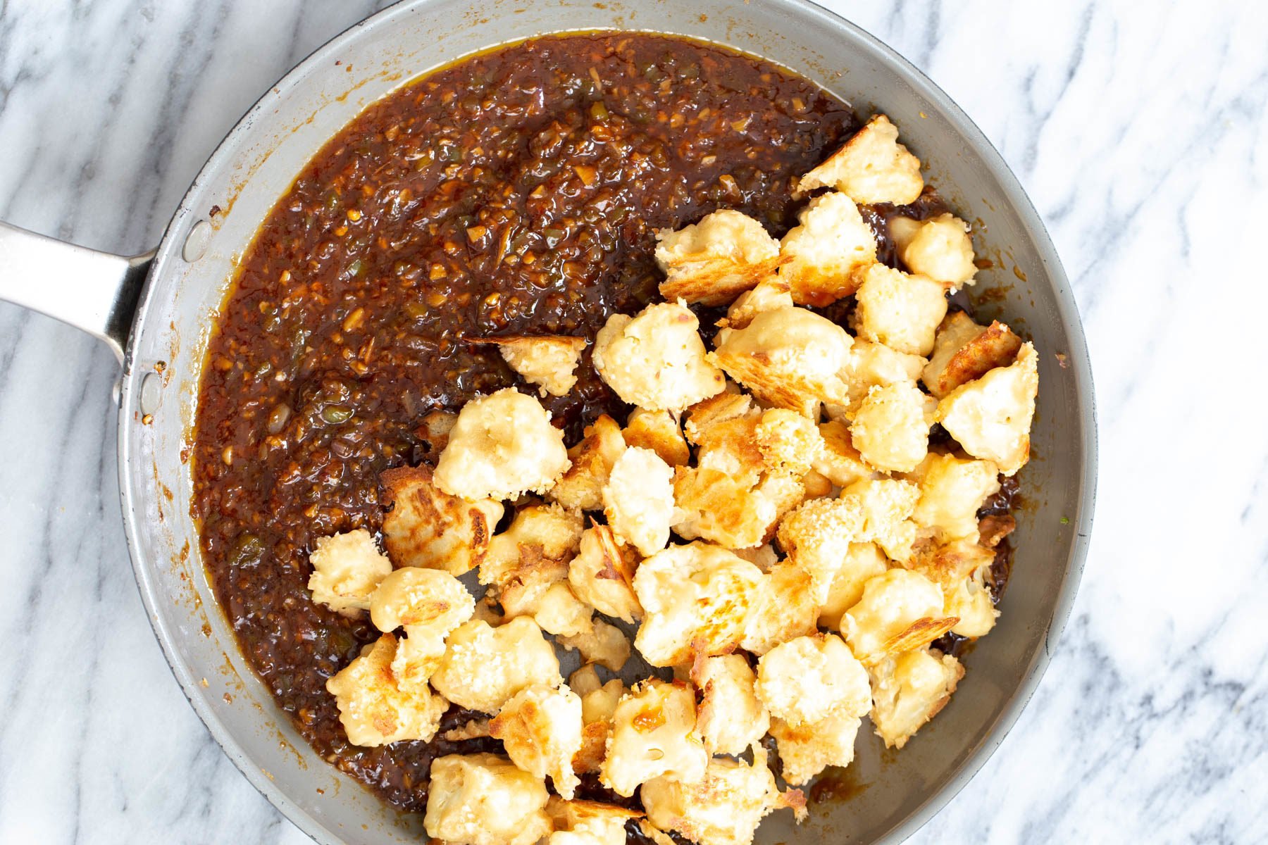 cauliflower manchurian  breaded baked cauliflower florets being added to Manchurian sauce in a pan