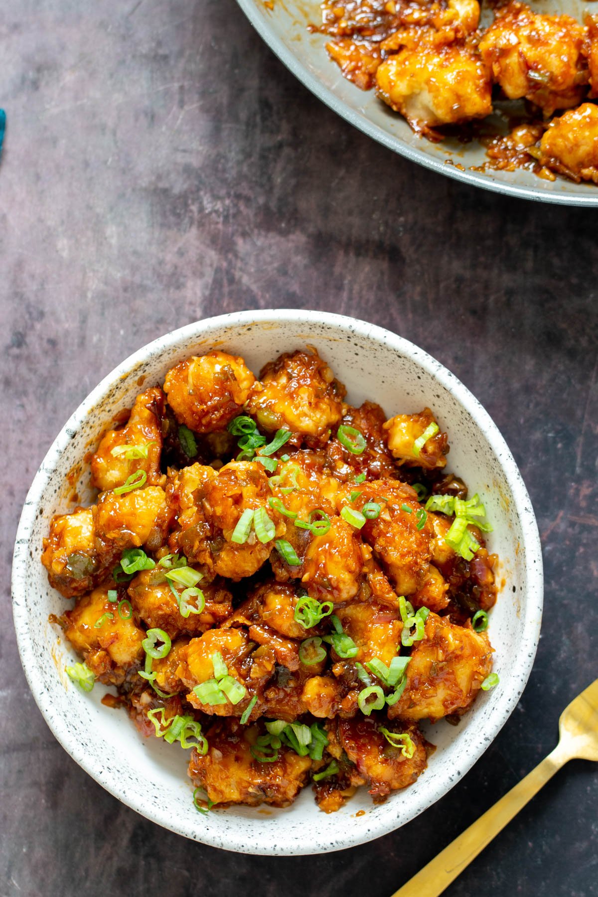 cauliflower manchurian  a serving of cauliflower manchurian in a white bowl with a golden fork on the side