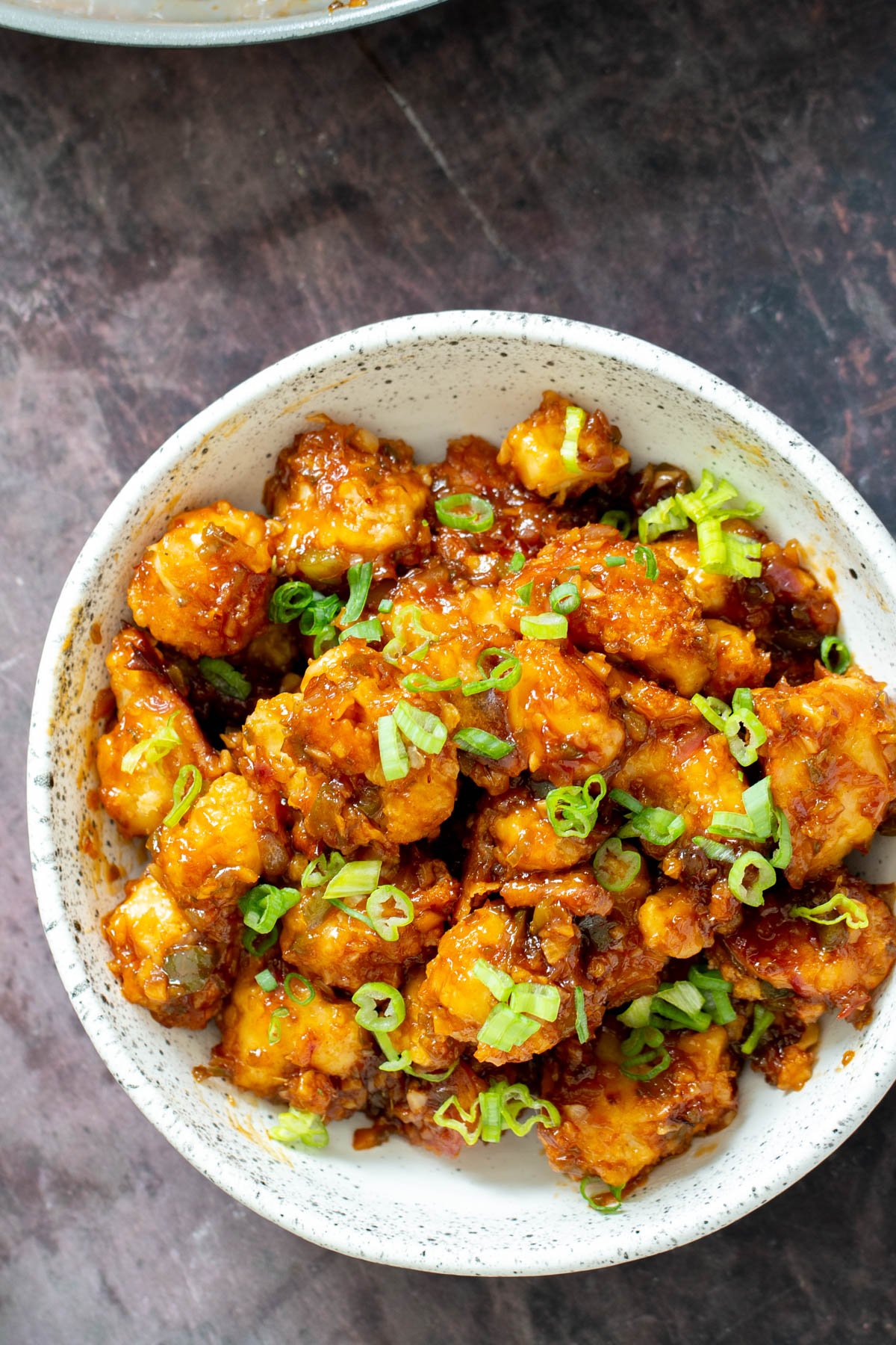 Cauliflower Manchurian  a white bowl with vegan gobi Manchurian topped with thinly sliced scallions