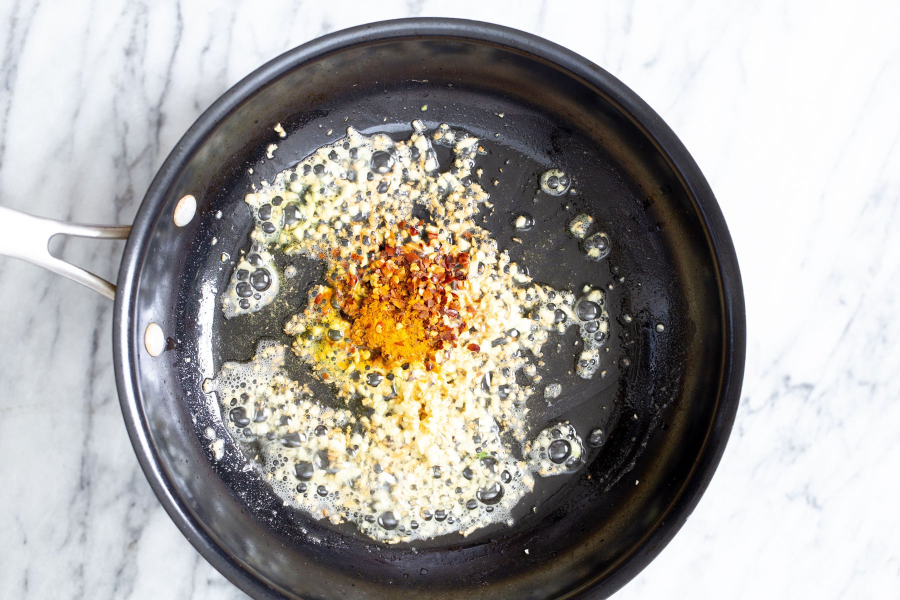 garlic pasta turmeric and pepper flakes being added to garlic in a frying pan