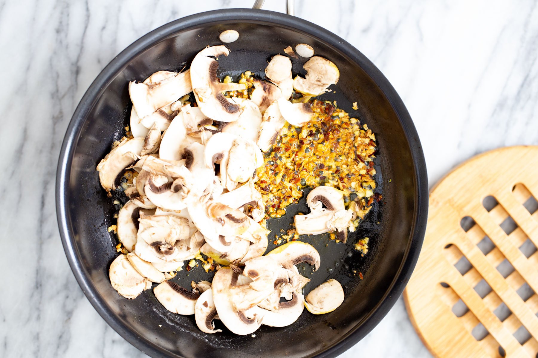 vegan garlic pasta sliced mushrooms being added to sauteed garlic in a frying pan