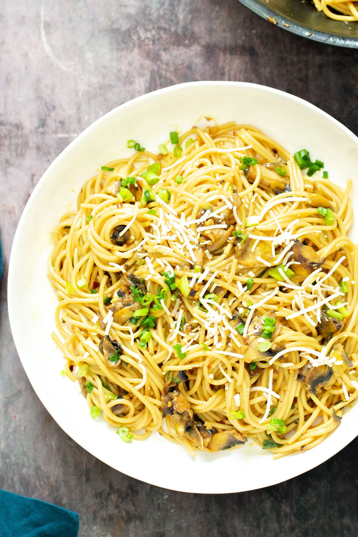 vegan garlic pasta a plate with vegan garlic pasta with mushrooms topped with vegan parmesan and scallions