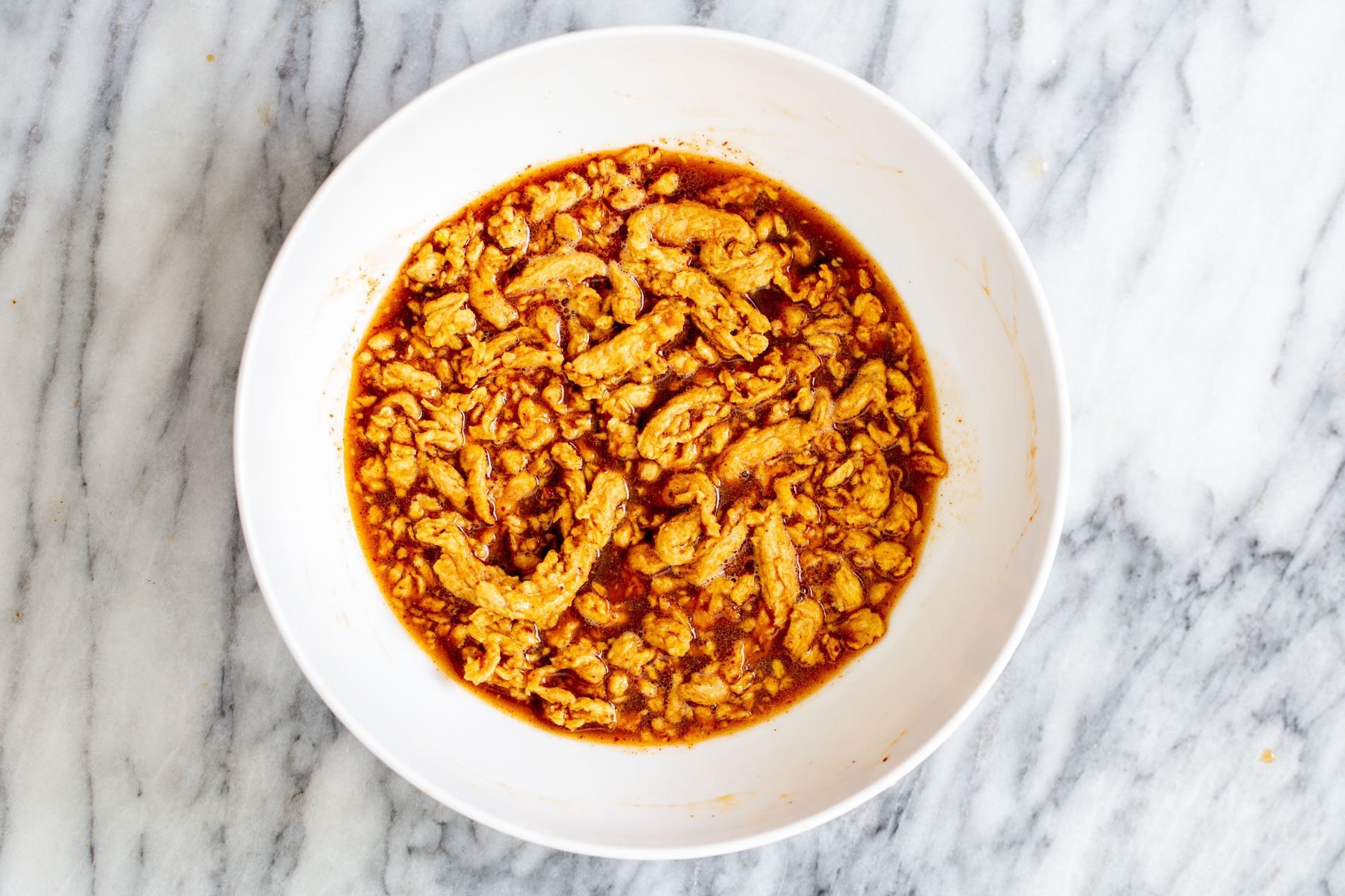 vegan crunchwrap  soy curls being marinated in korean bbq marinade in a white bowl