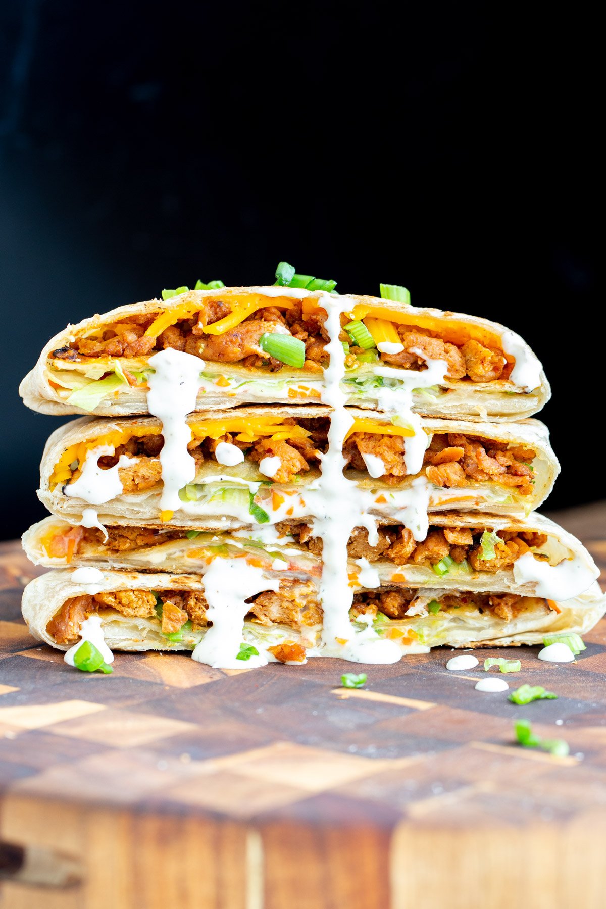 vegan crunchwrap halved vegan crunchwraps stacked on a wooden board drizzled with vegan ranch