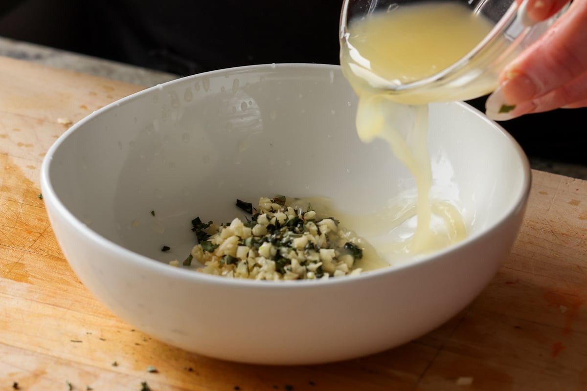 adding lemon juice to the garlic and herbs in a bowl