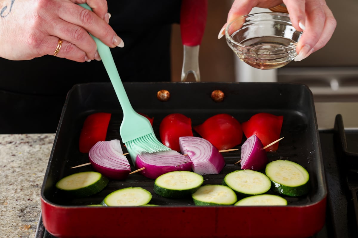 adding the vegetables to a grill pan, brushing with oil