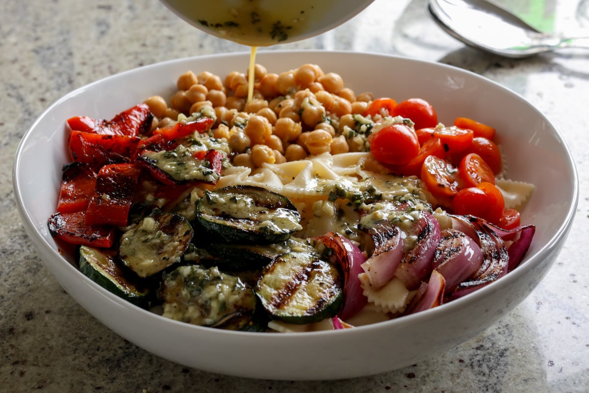adding Italian dressing to chickpeas, pasta, and grilled vegetables in the mixing bowl before mixing