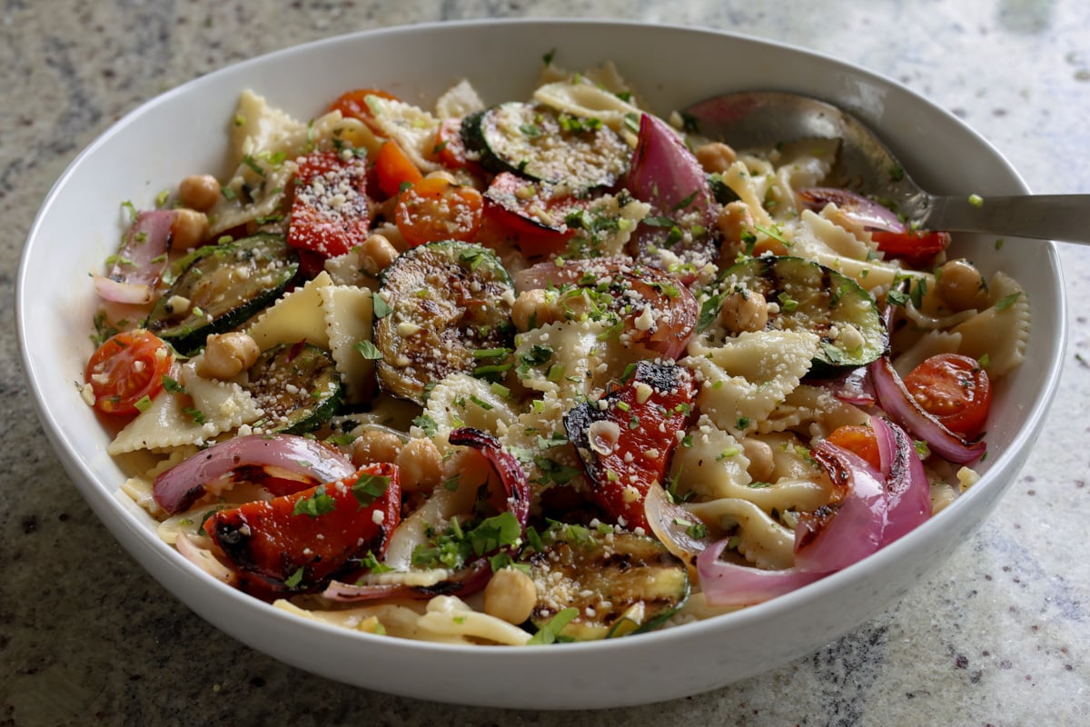 chickpeas, pasta, and grilled vegetables in the mixing bowl after mixing and sprinkling with vegan parmesan