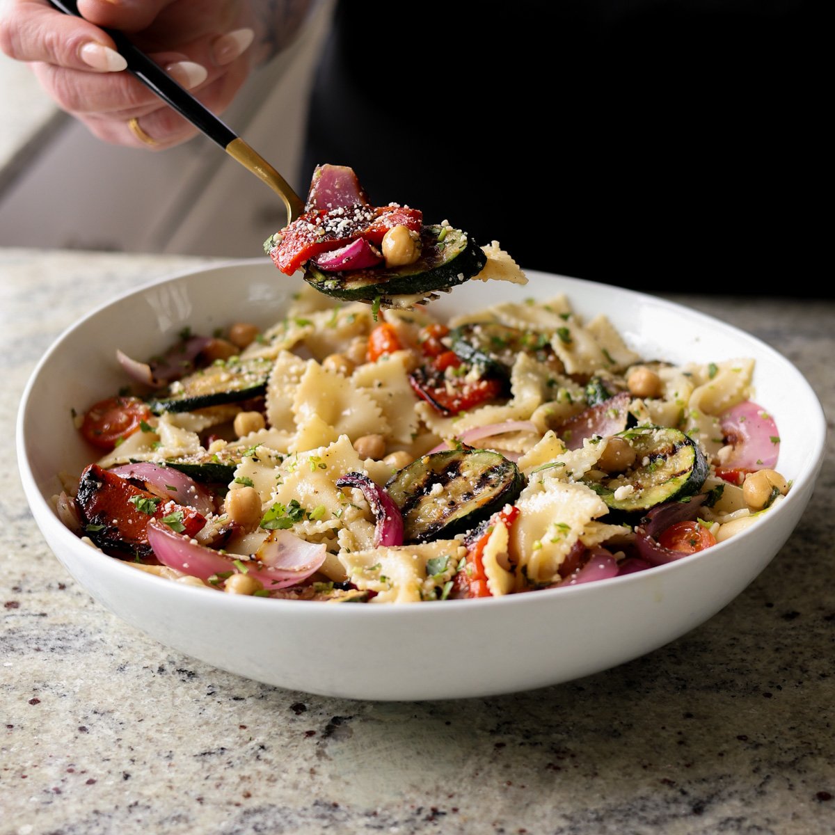 spooning a bite of summer pasta salad with grilled vegetables