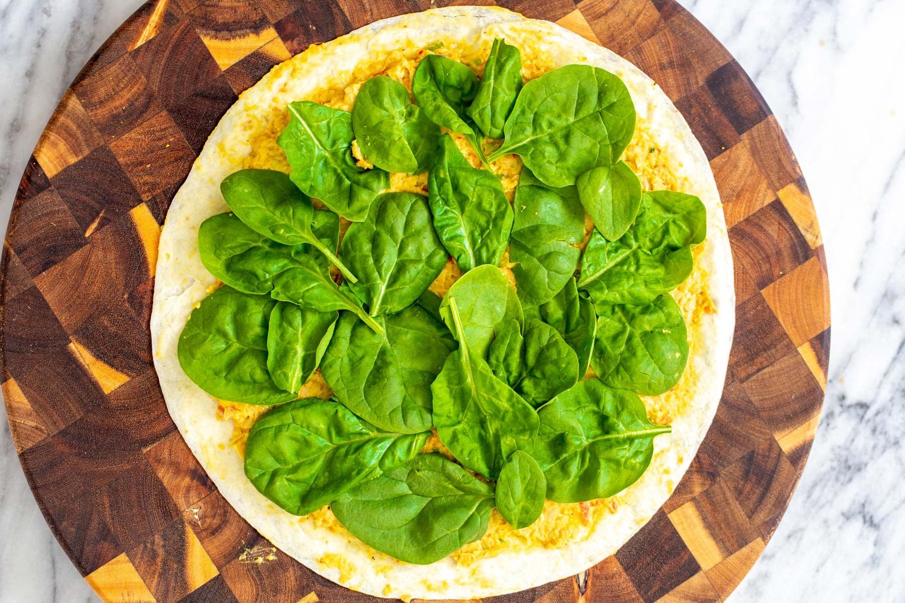 chickpea breakfast  tortilla topped with chickpea scramble and fresh spinach on a wooden board