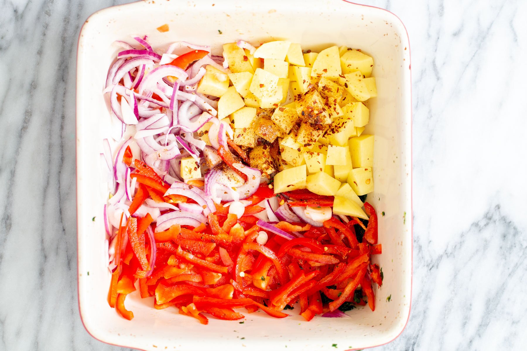 sliced onion and bell pepper and cubed potatoes in a white casserole dish