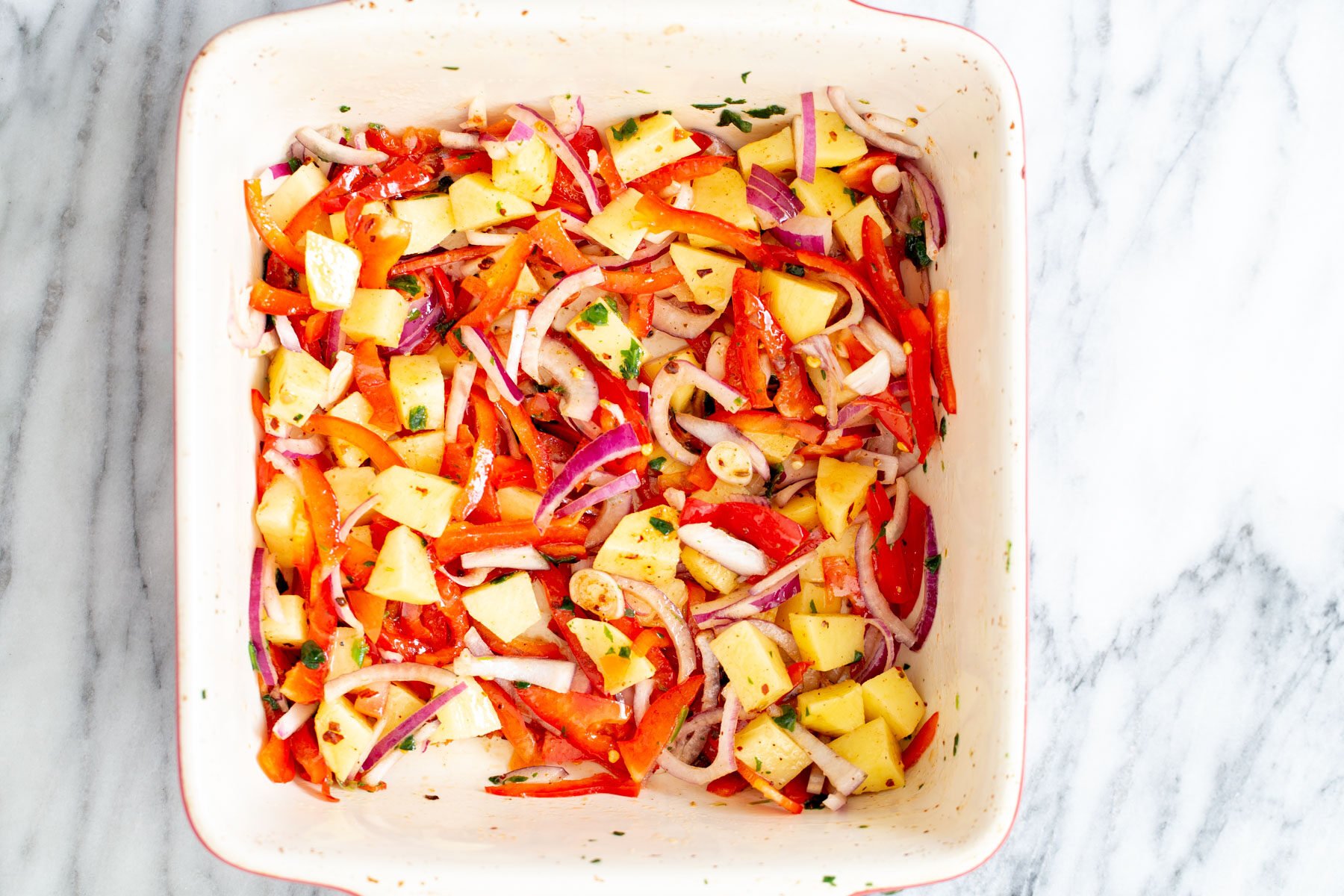 vegan Mexican casserole vegetables mixed with seasoning and oil in a white baking dish