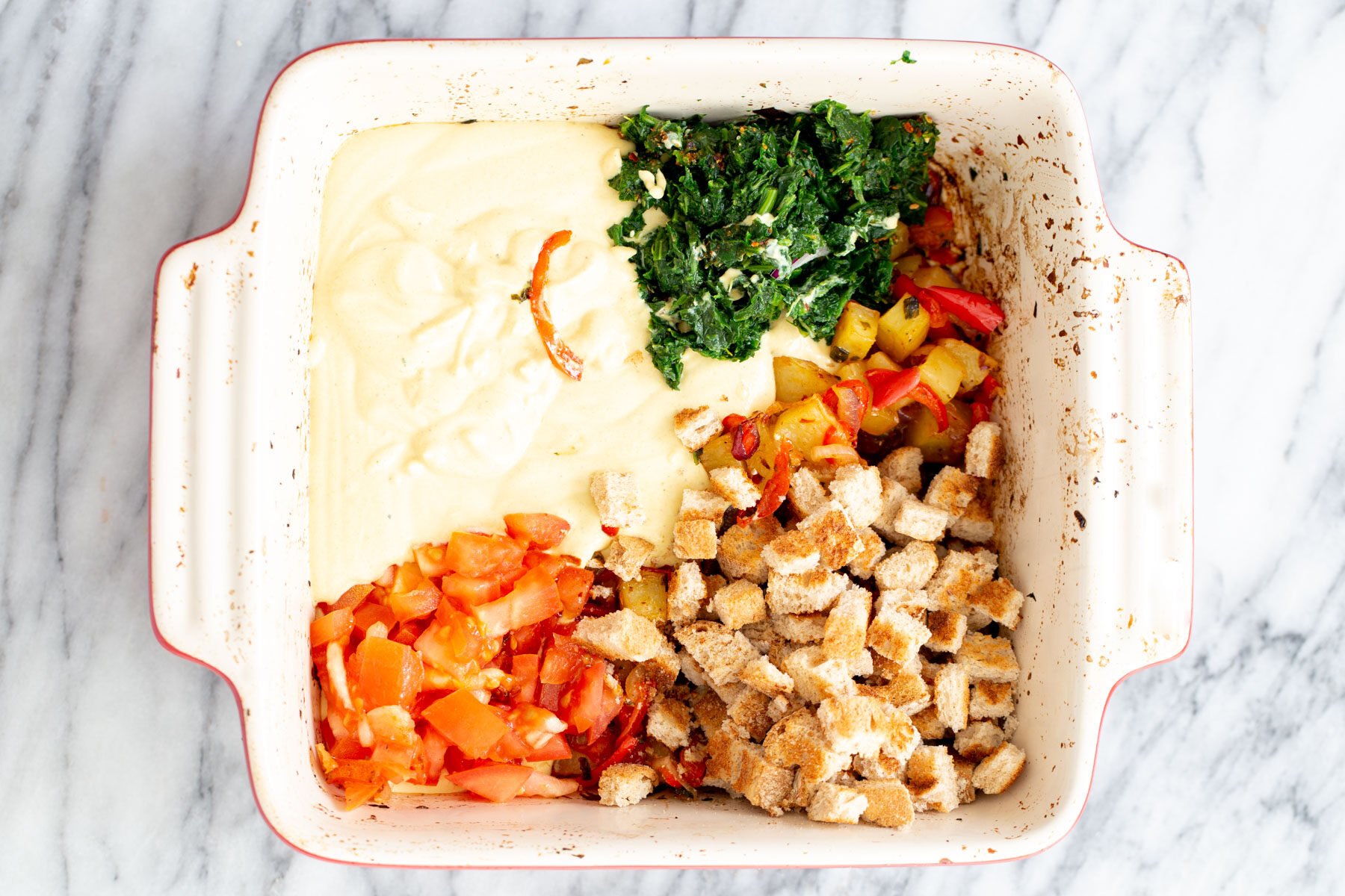 bread cubes, fresh spinach and tomatoes being added to egg casserole