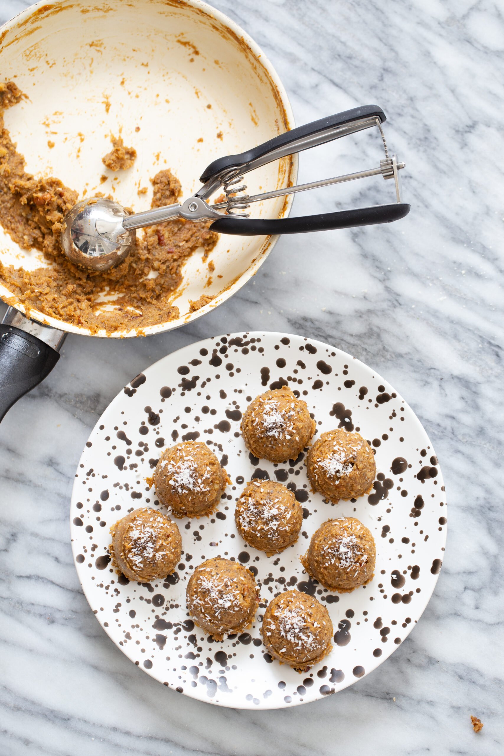 pumpkin pie energy balls on a white plate with cookie scoop in a skillet