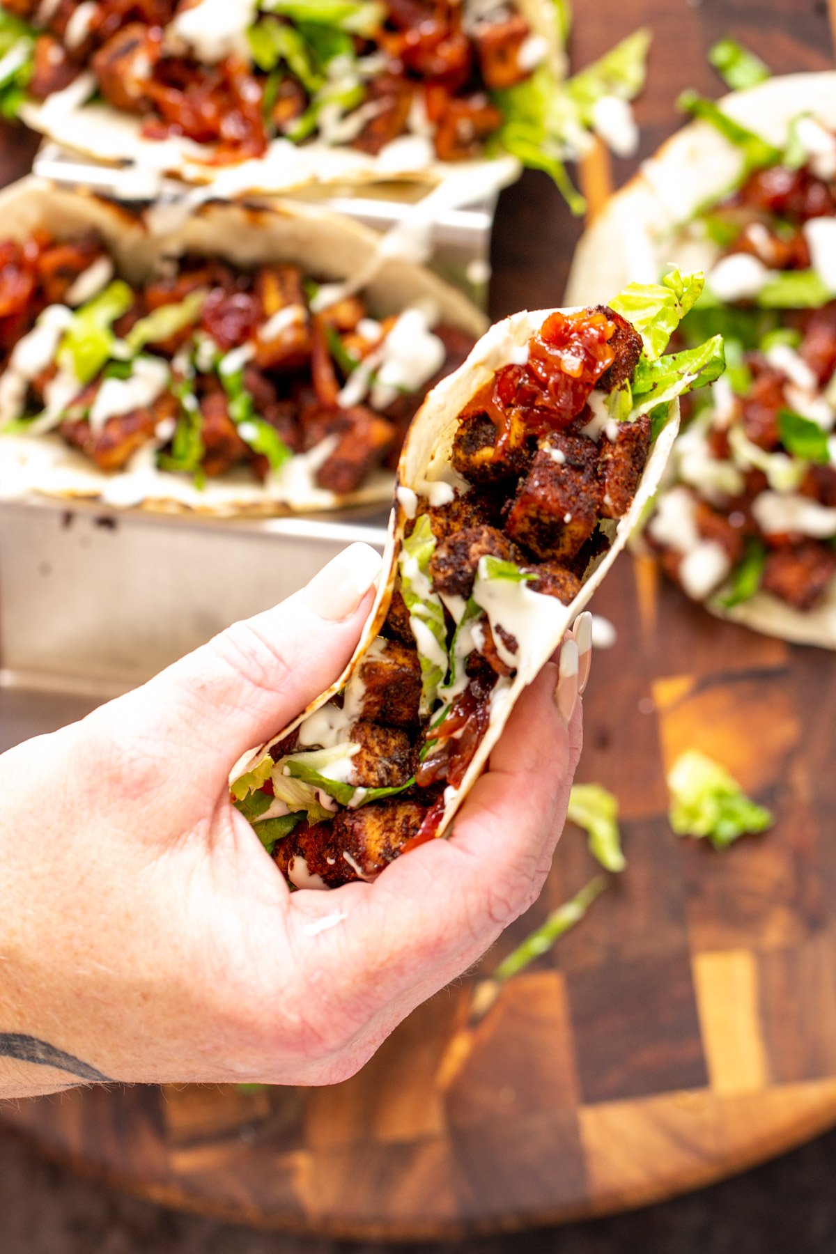 blackened tofu tacos  a hand holding a vegan blackened tofu taco drizzled with sour cream and filled with caramelized onions