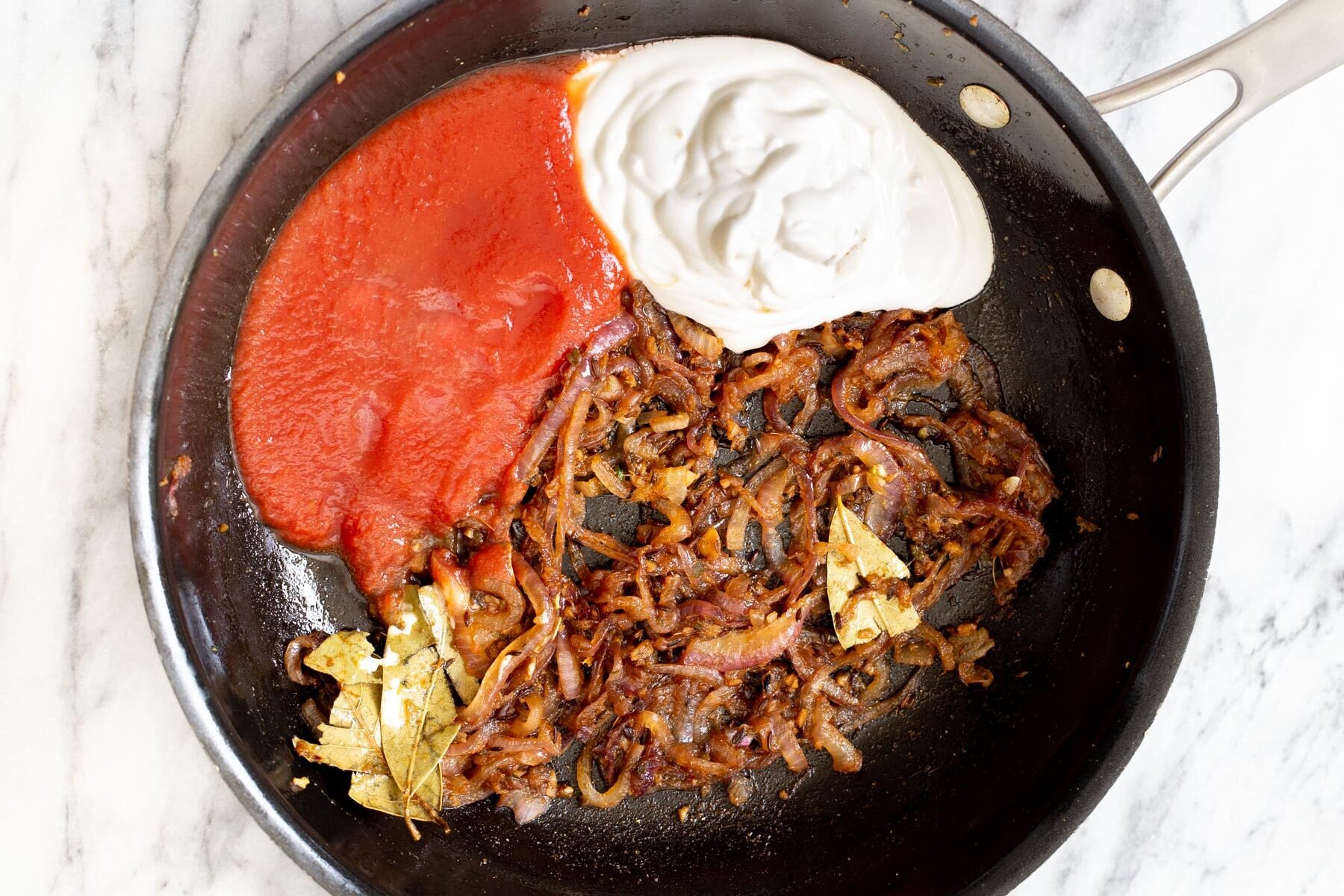 tomato puree and yogurt being added to make Indian gravy in a sauteeing pan