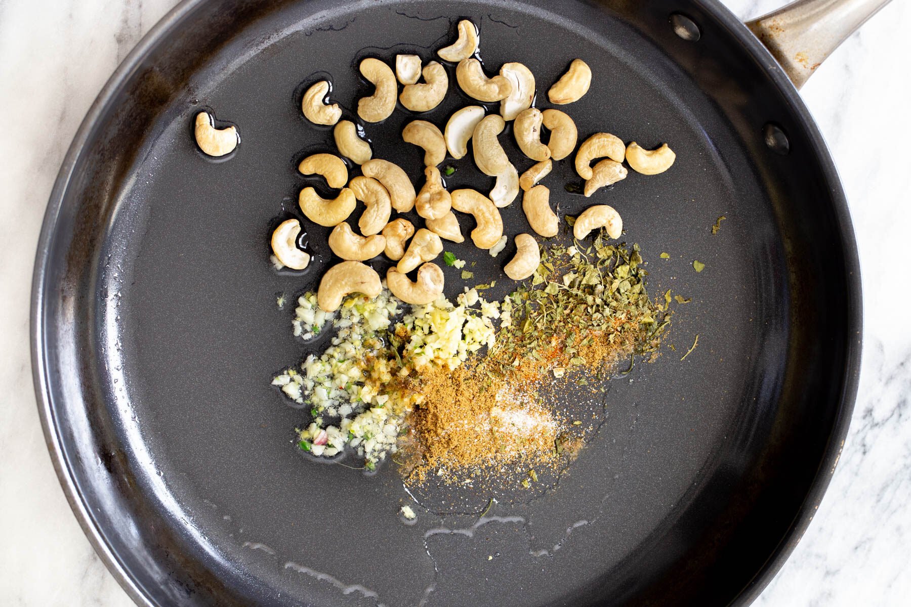 cashew nuts, garlic, and spices in a black frying pan