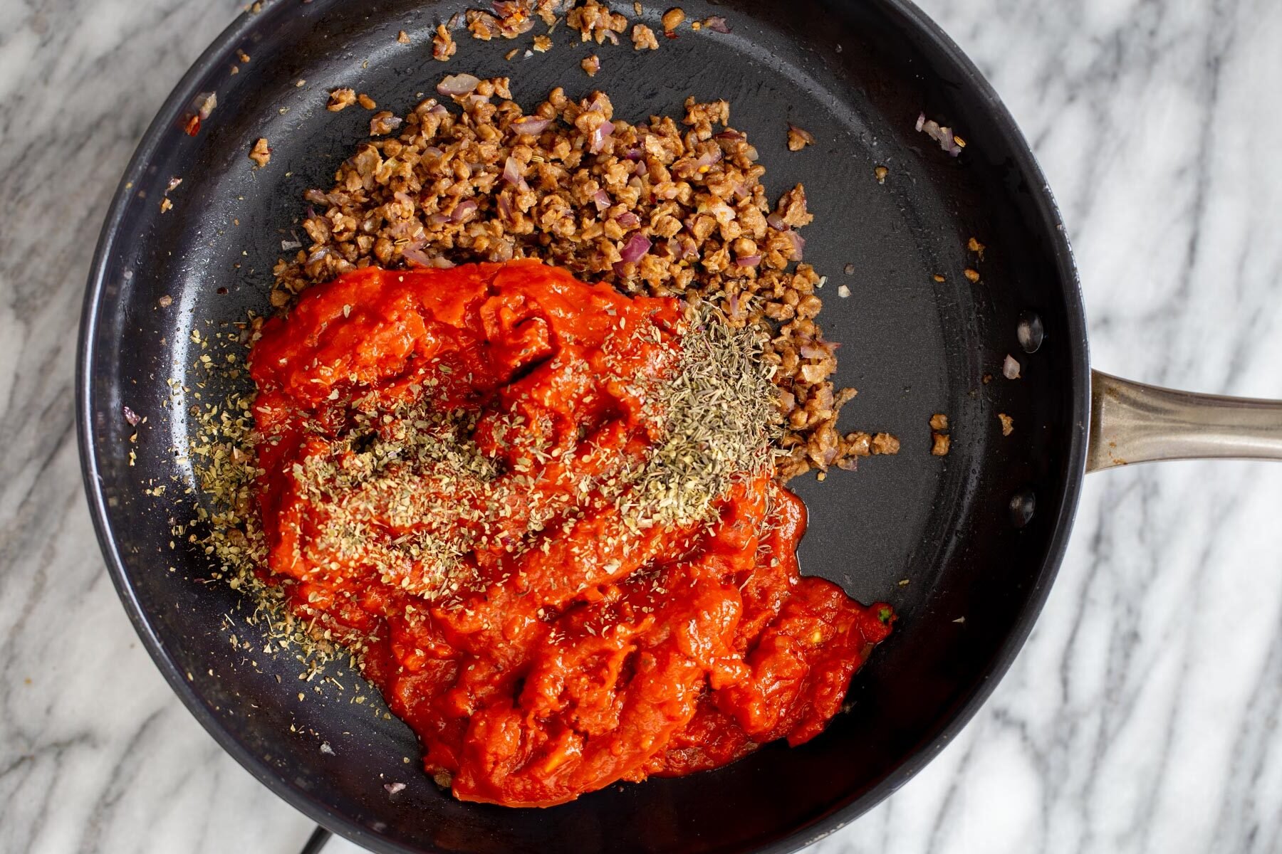 vegan skillet lasagna tomato sauce being added to a skillet with vegan meat crumbles