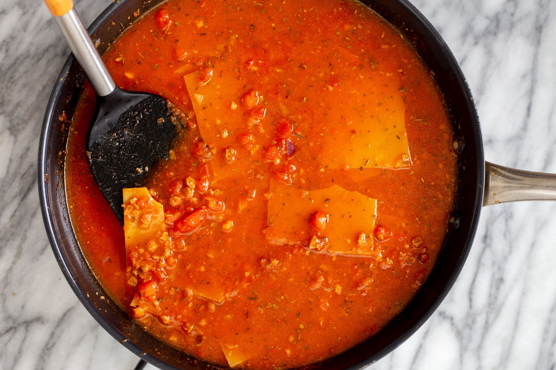 vegan skillet lasagna broked lasagna noodles being added to marinara sauce in a skillet