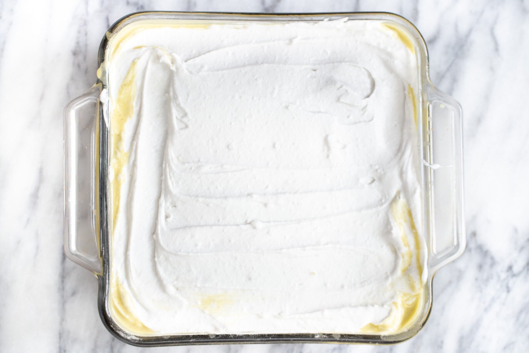 vegan coconut whip being spread over a soaked sponge cake to make tres leches