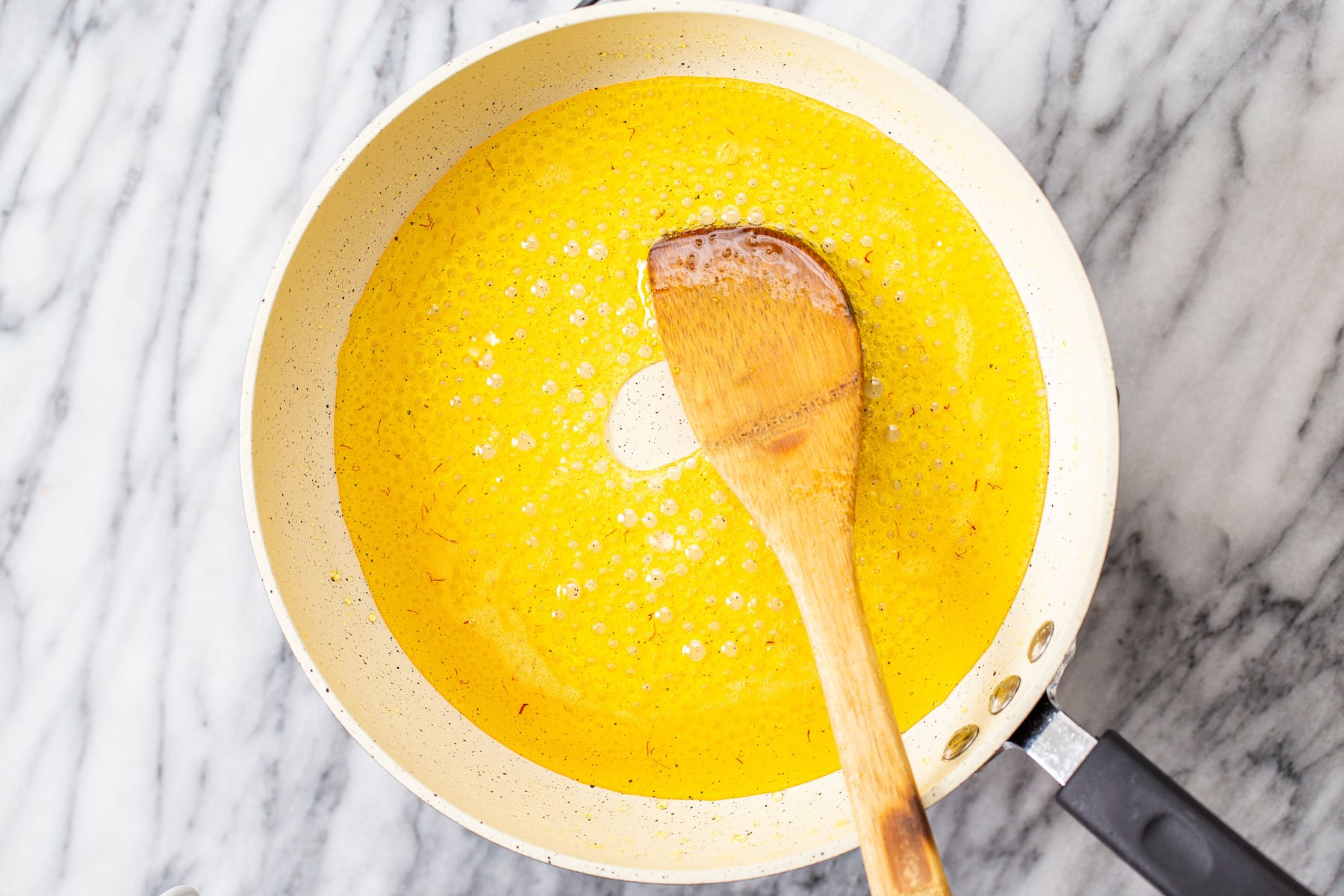 saffron, butter, water and sugar being melted in a saucepan to make almond burfi
