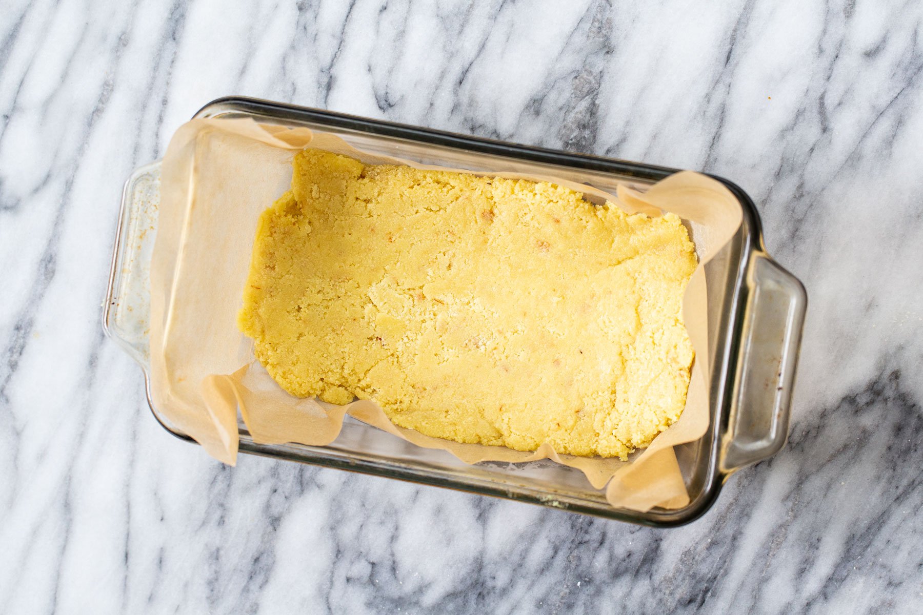 almond burfi mix being pressed into a pyrex loaf pan