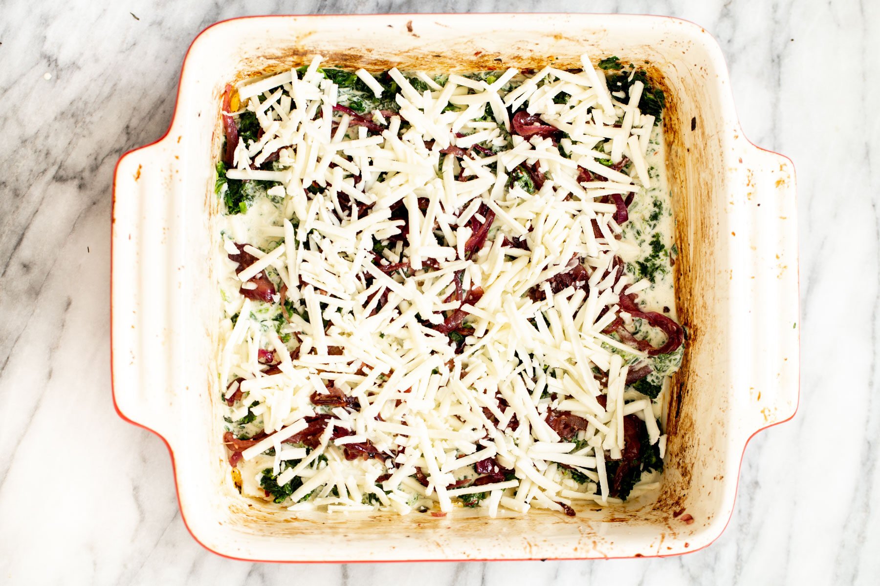 vegan butternut lasagna being topped with vegan cheese shreds