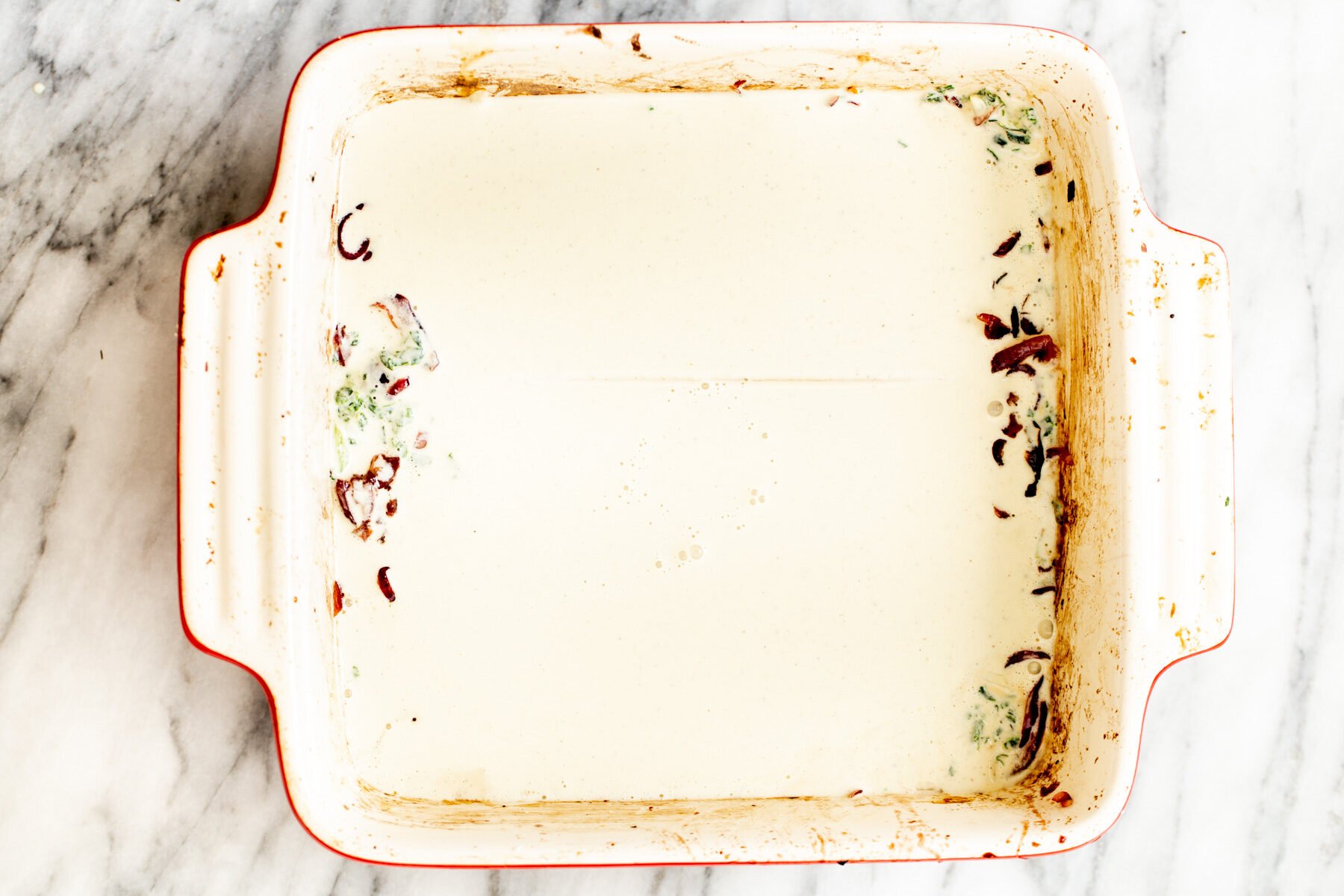 vegan bechamel being poured over lasagna noodles to make butternut squash lasagna