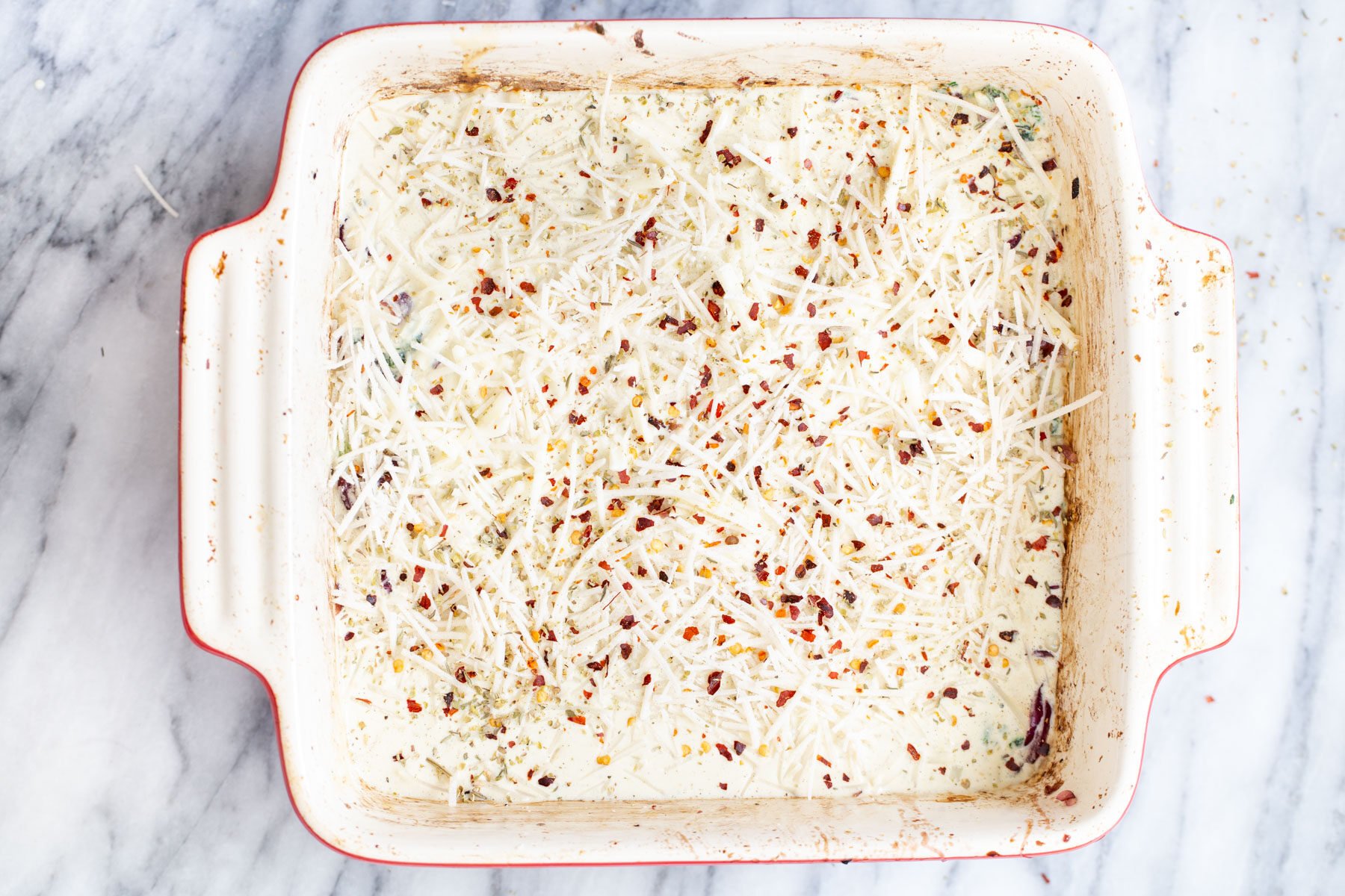 cheese shreds and pepper flakes being added over lasagna noodles
