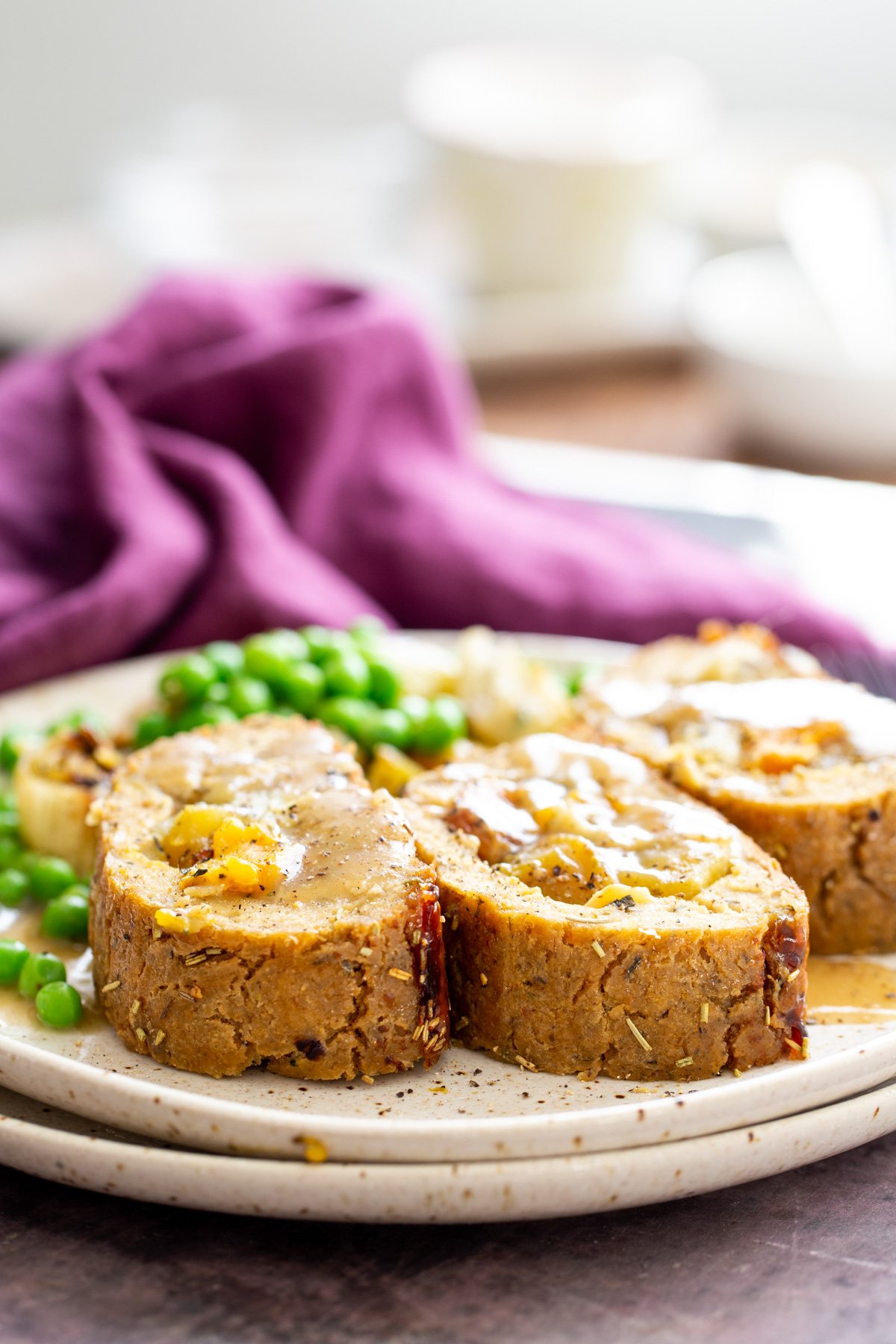 glutenfree holiday roast three slices of vegan glutenfree holiday loaf drizzled with gravy with a side of vegetables in the background