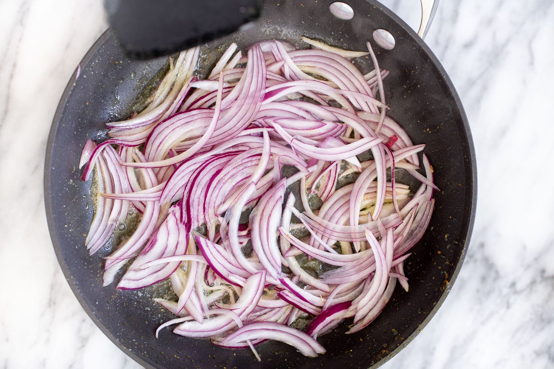 onion sliced in a black sauteeing pan
