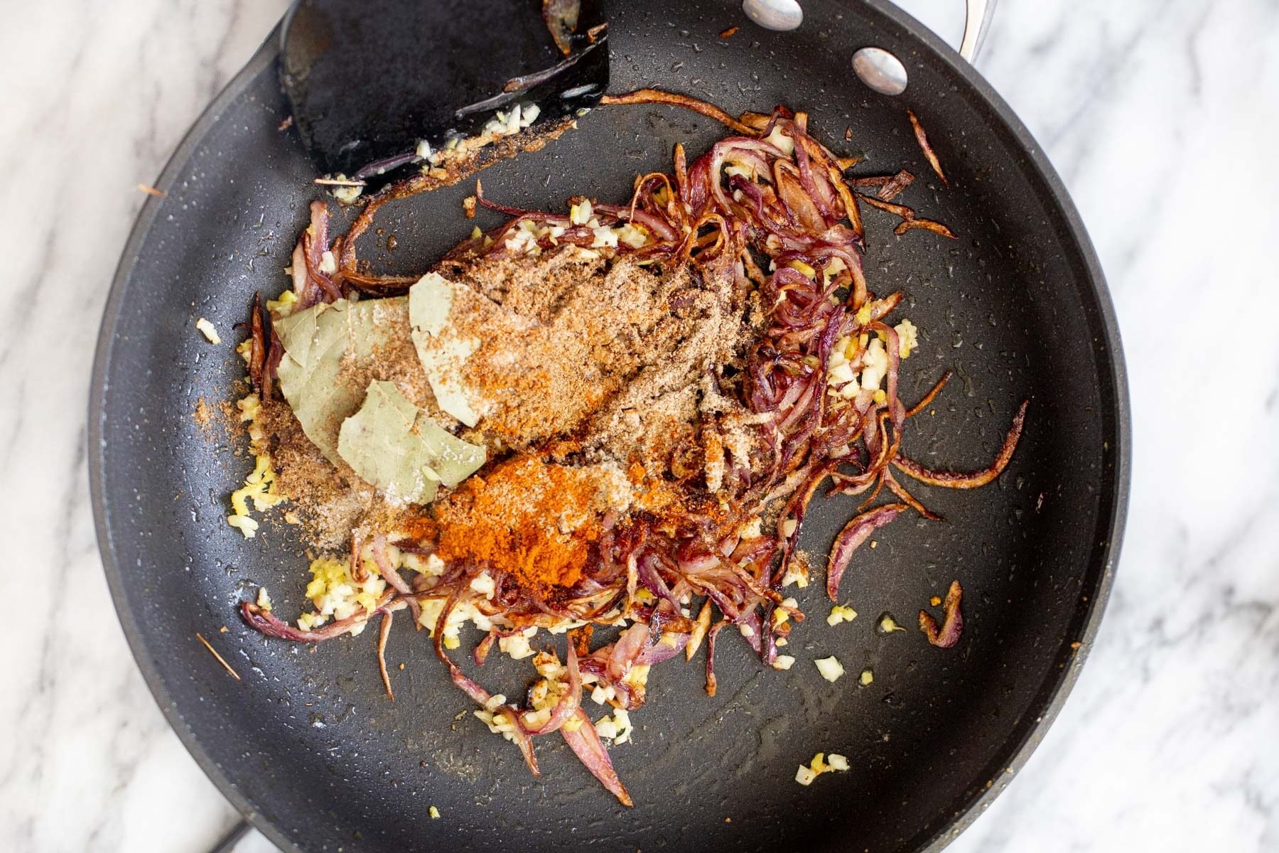 onion and garlic being tempered with spices in a black skillet