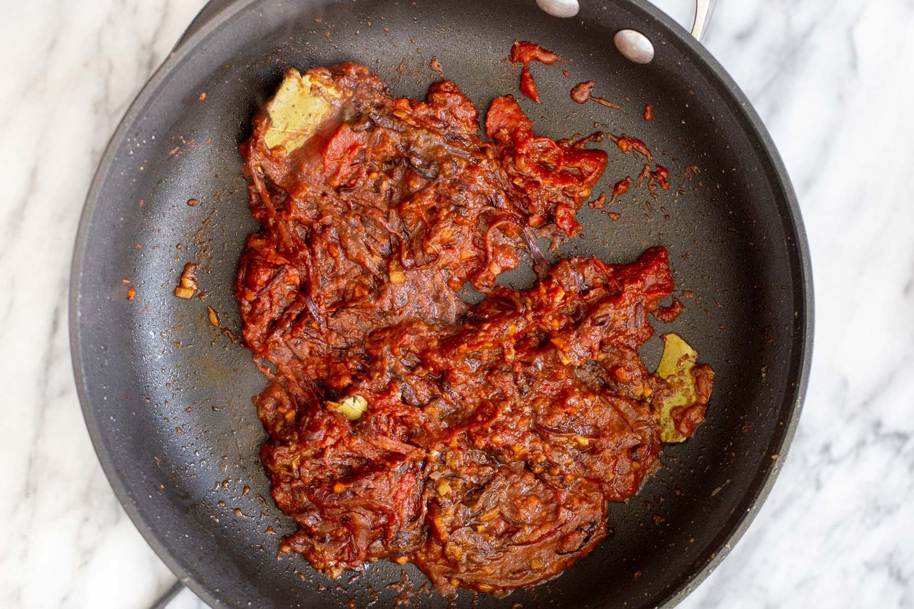 tomato paste being added to onion garlic mix in a sauteeing pan
