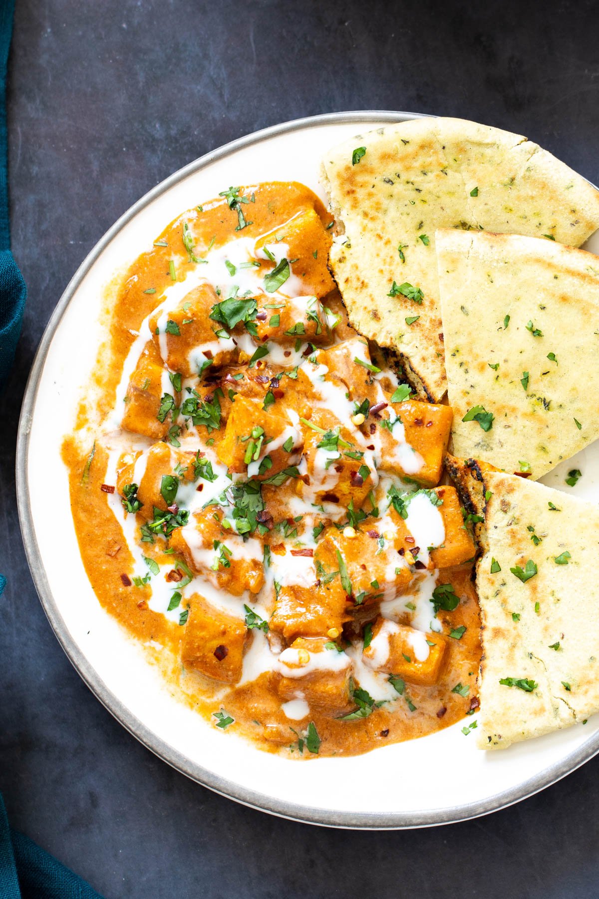 Indian Malai Tofu curry with naan bread on a white plate