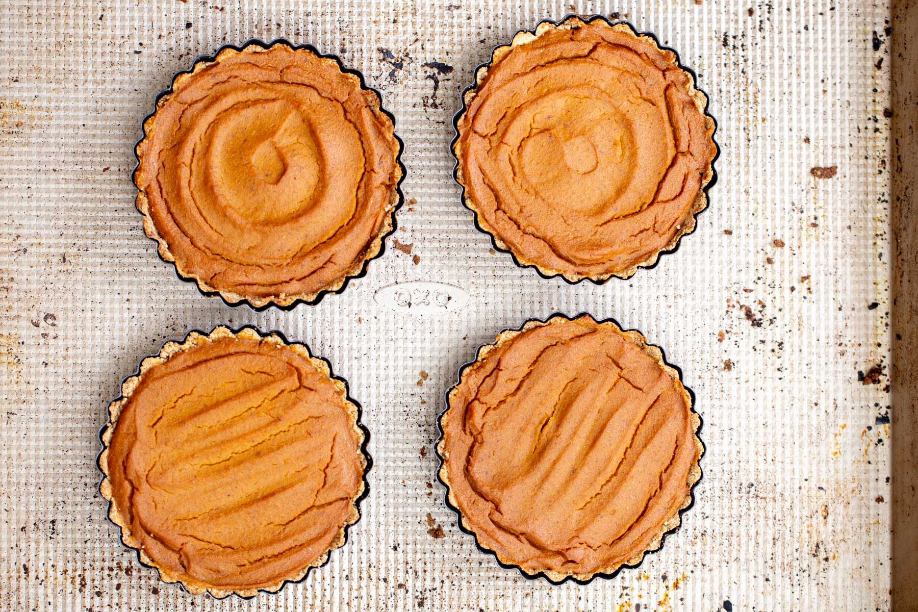 four gluten free vegan pumpkin pies on a baking sheet