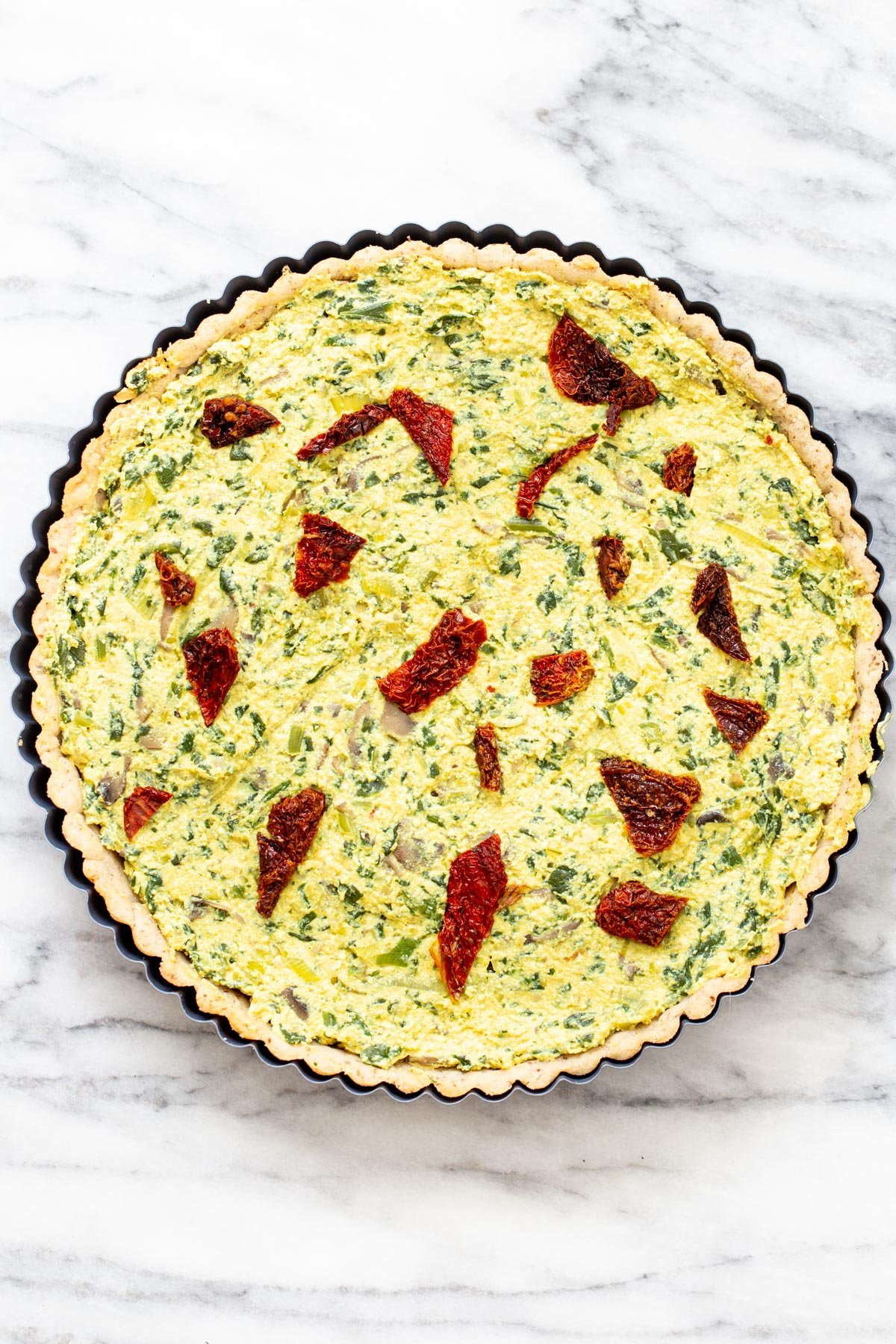 unbaked vegan quiche with mushrooms, spinach and leeks in a tart pan