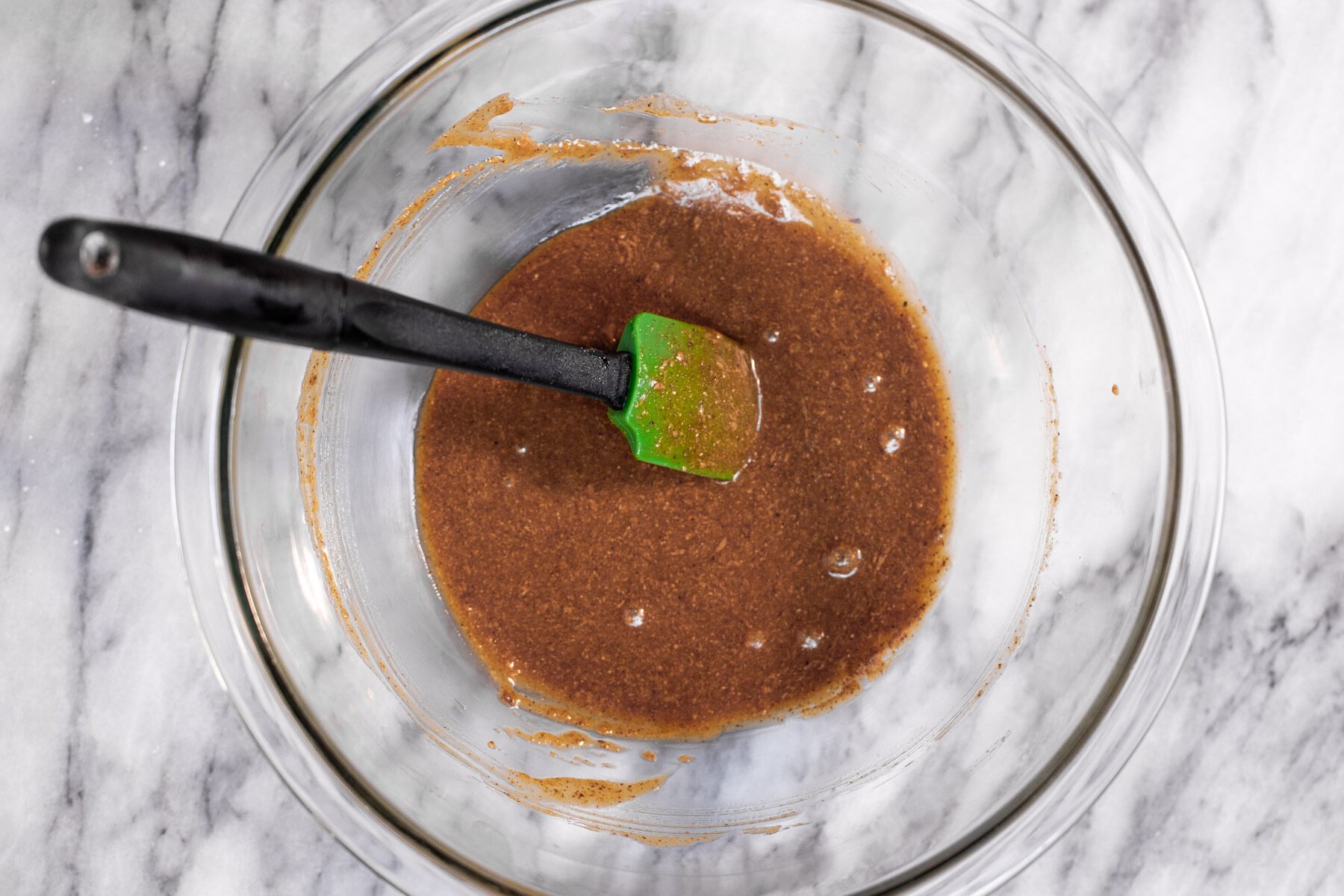 almond butter being mixed with maple syrup, vanilla and oil in a glass bowl