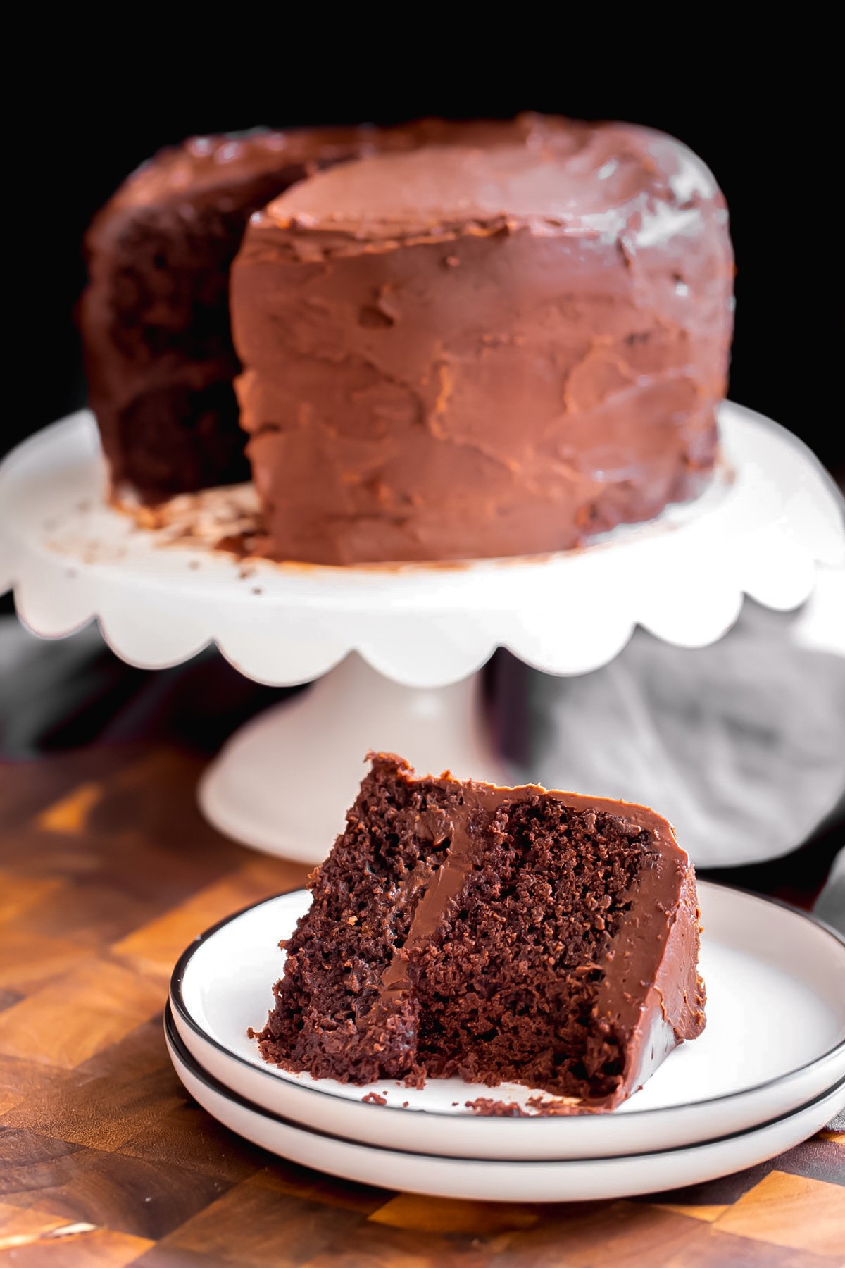 a slice of vegan glutenfree chocolate layer cake on a white plate in front of a cake on a cake platter