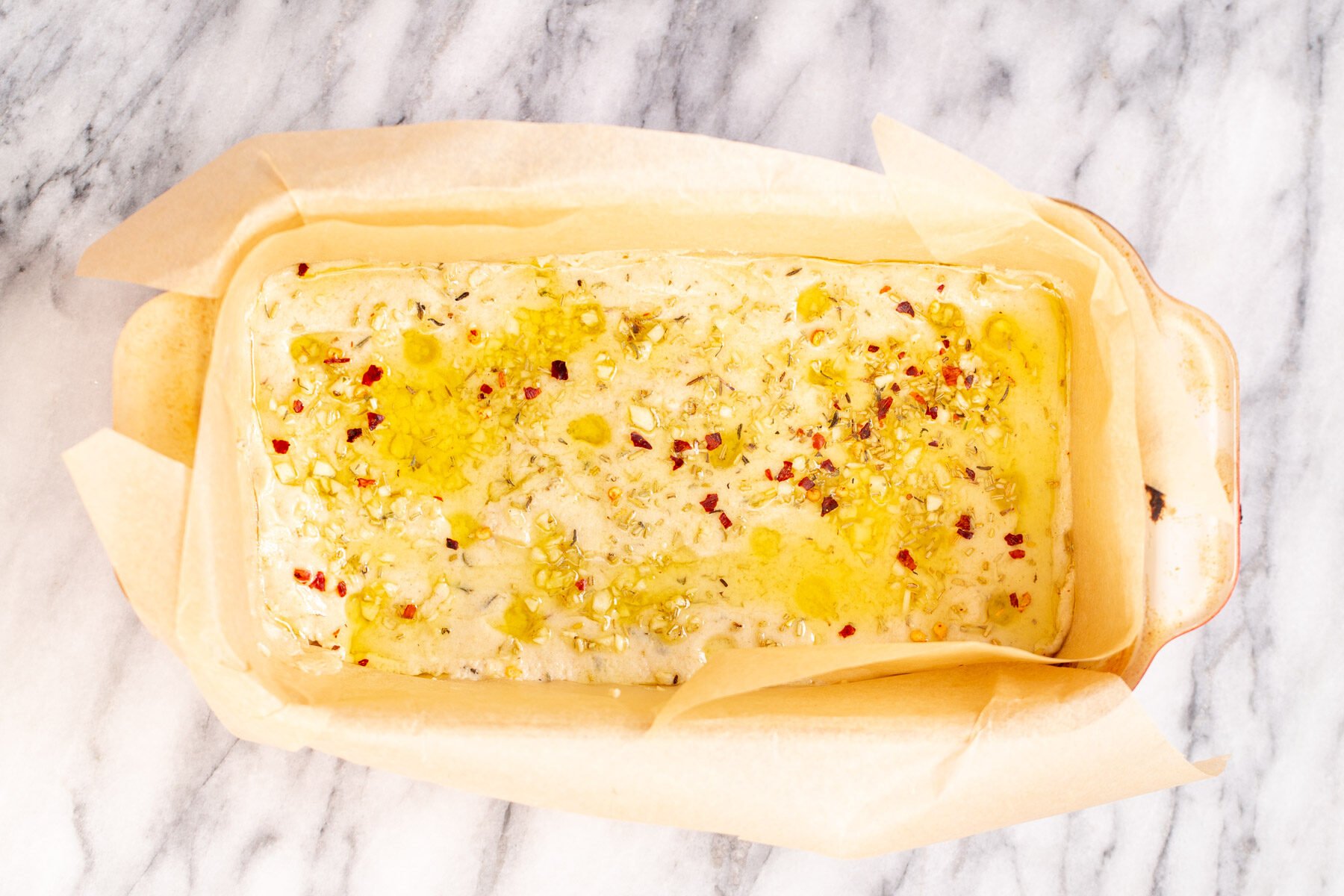 vegan glutenfree focaccia in a bread pan covered with olive oil garlic and spices