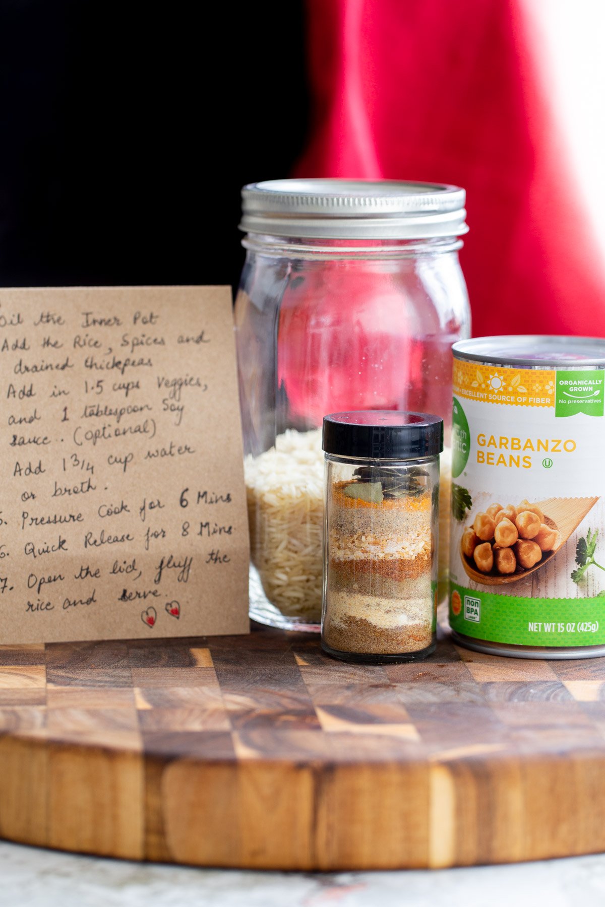 a recipe card, spice mix, can of chickpeas and a mason jar with rice on a wooden board