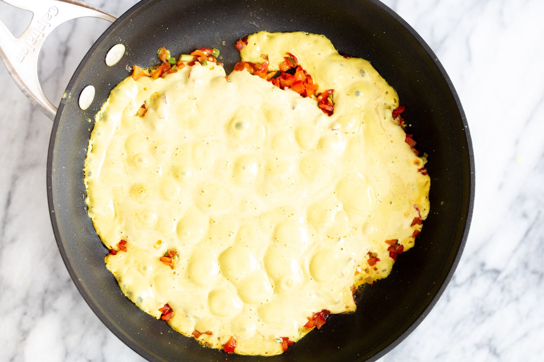 tofu scramble seasoning vegan tofu egg mixture being poured in a pan with sauteed vegetables
