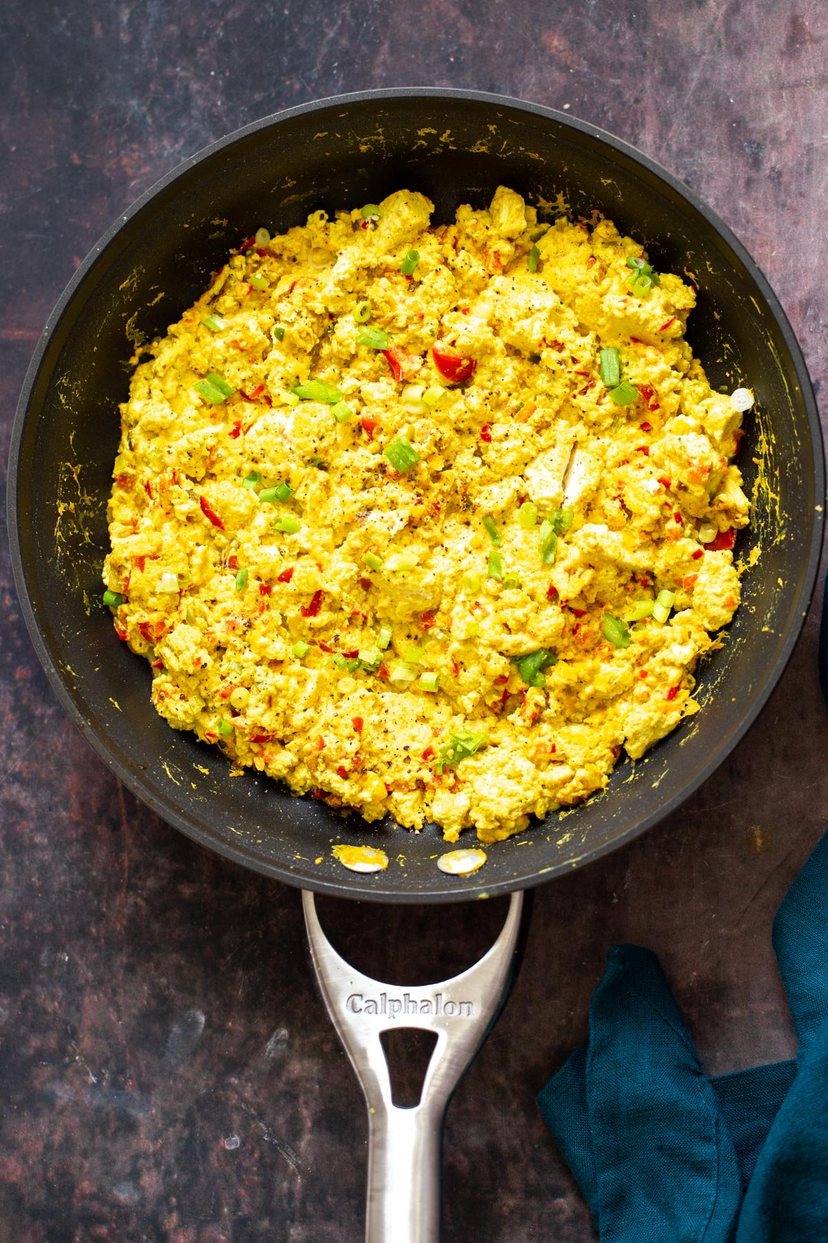 tofu scramble seasoning a black skillet with vegan tofu scramble with bell peppers and green onions