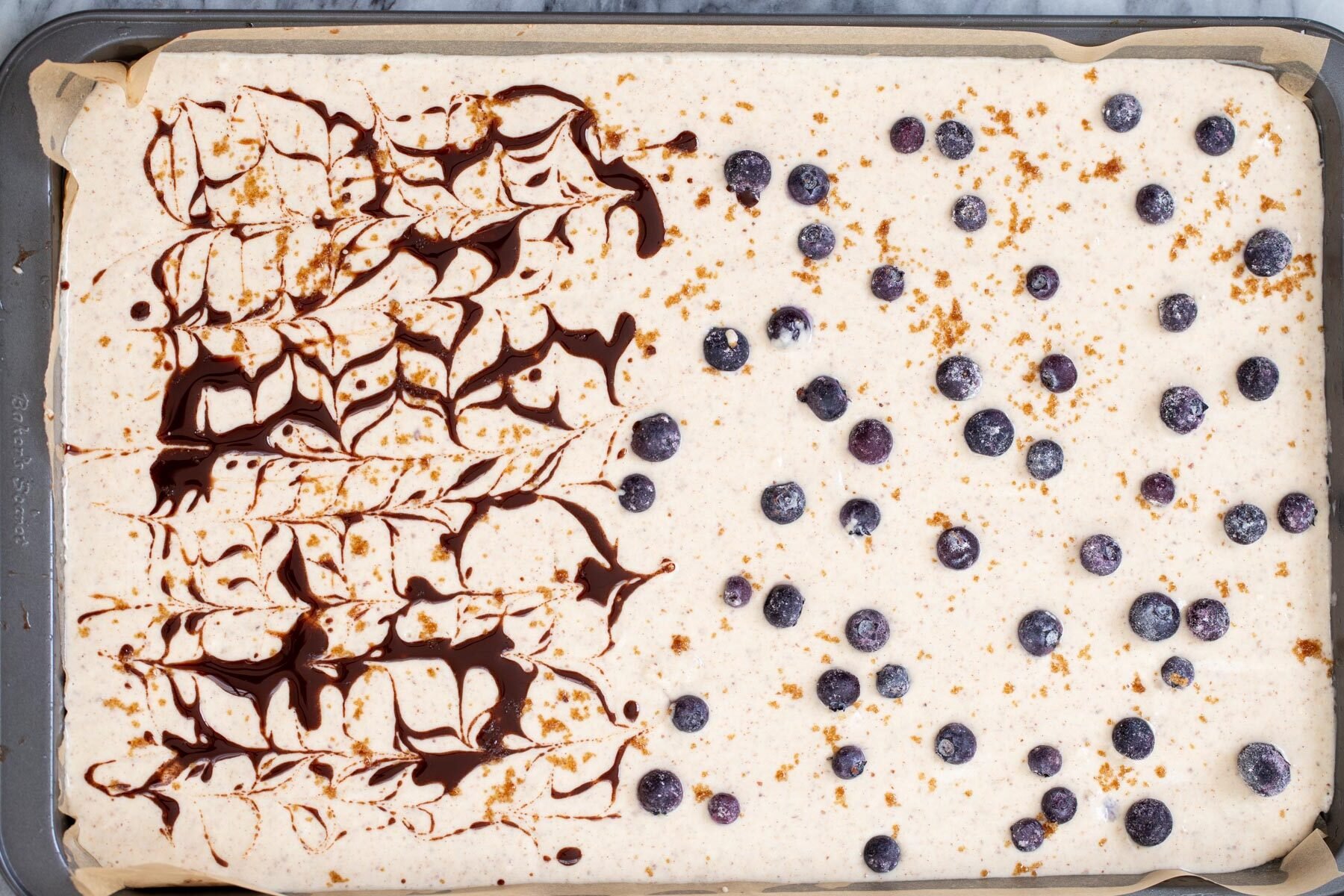 a sheet pan with pancake batter half topped with blueberries, half swirled with cinnamon syrup 