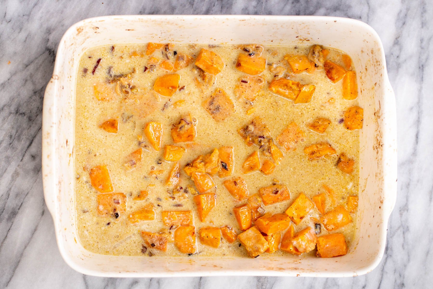 a casserole dish with sweet potatoes baking in coconut milk gravy