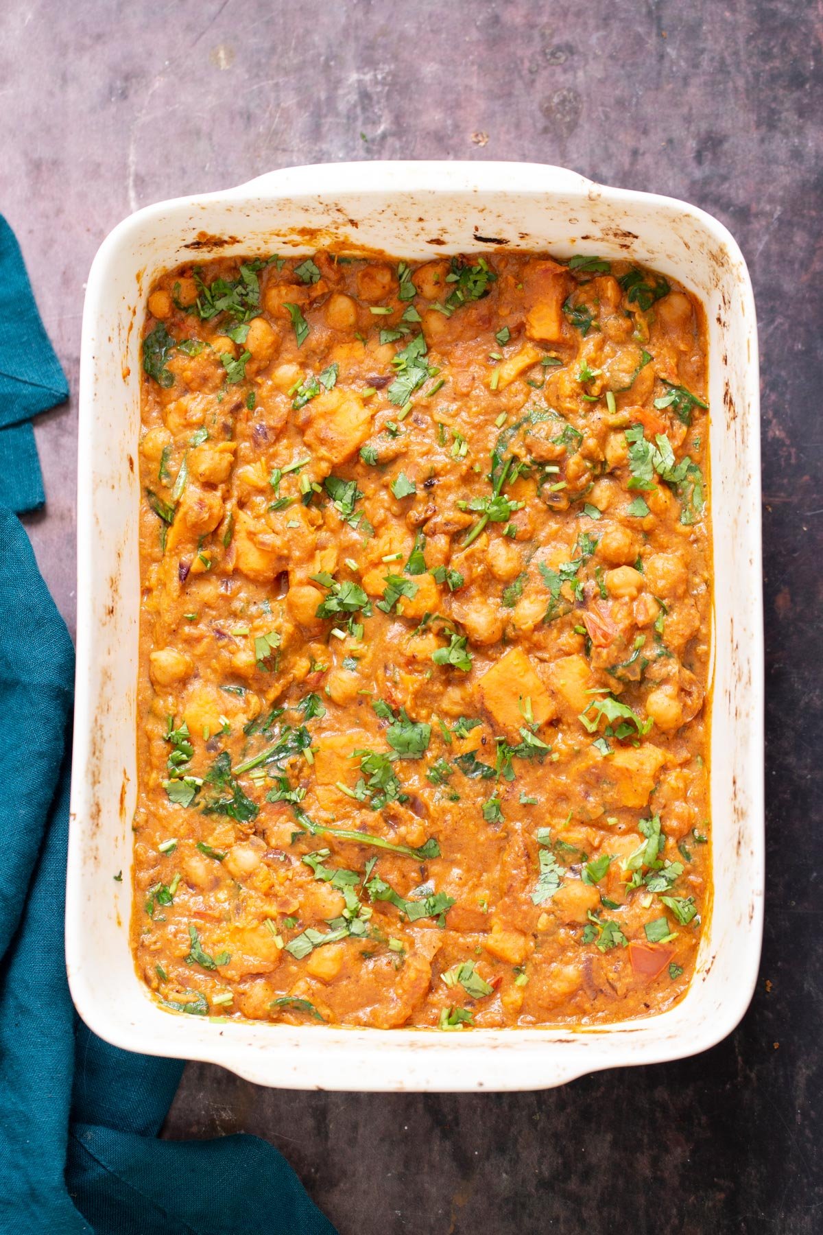 Top shot of casserole dish with chickpea sweet potato curry, blue green kitchen napkin on the side