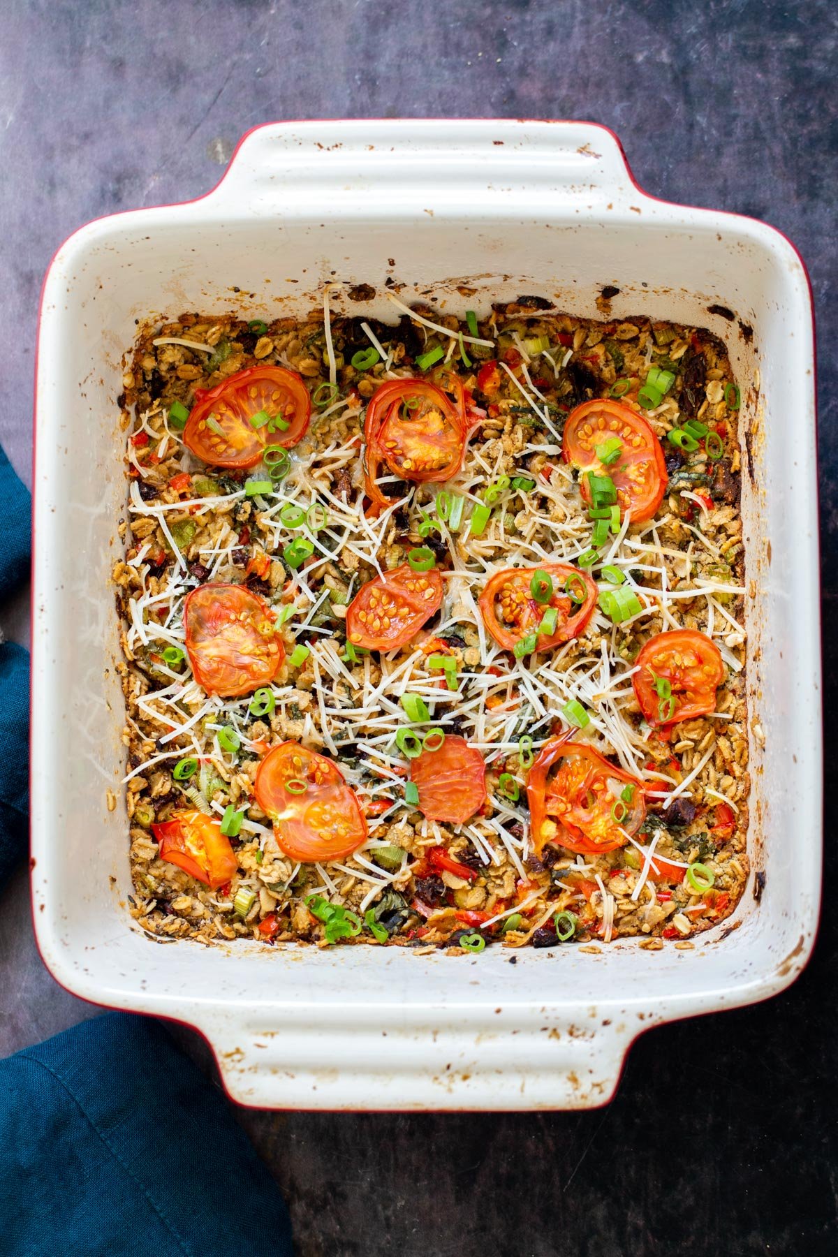 a casserole dish with savory pizza oatmeal bake topped with shredded mozarella and tomatoes