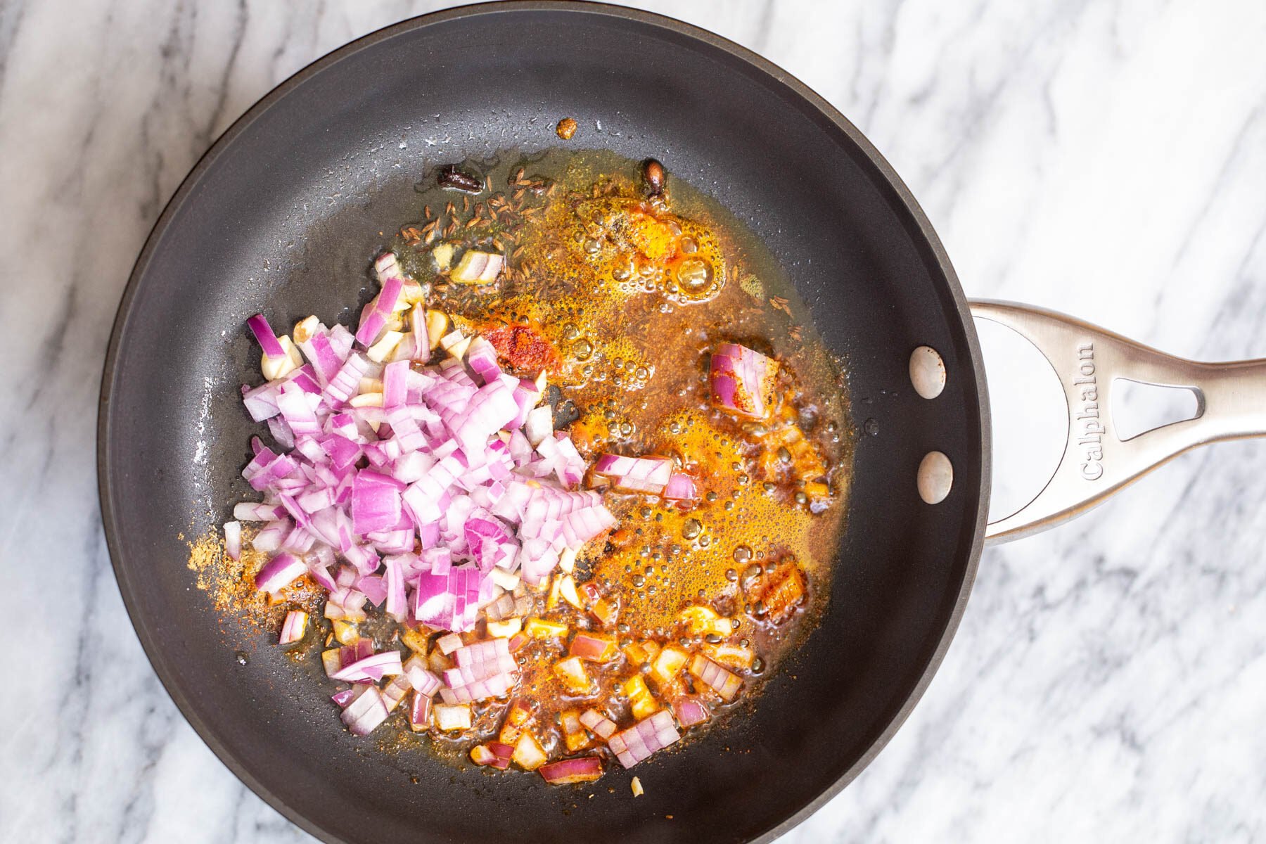 chopped red onion being added to tempering to make ural dal