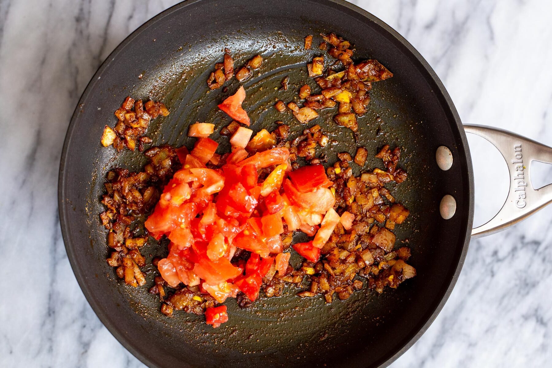 fresh tomatoes being added to skillet with onions and spices
